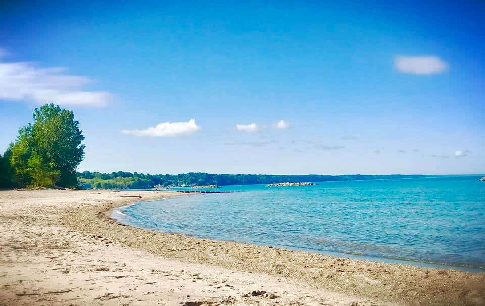 Lake Erie 桌布 壁紙 — 在晴朗藍天與散落雲朵下，一條寧靜的沙灘沿著碧綠海水蜿蜒伸展。