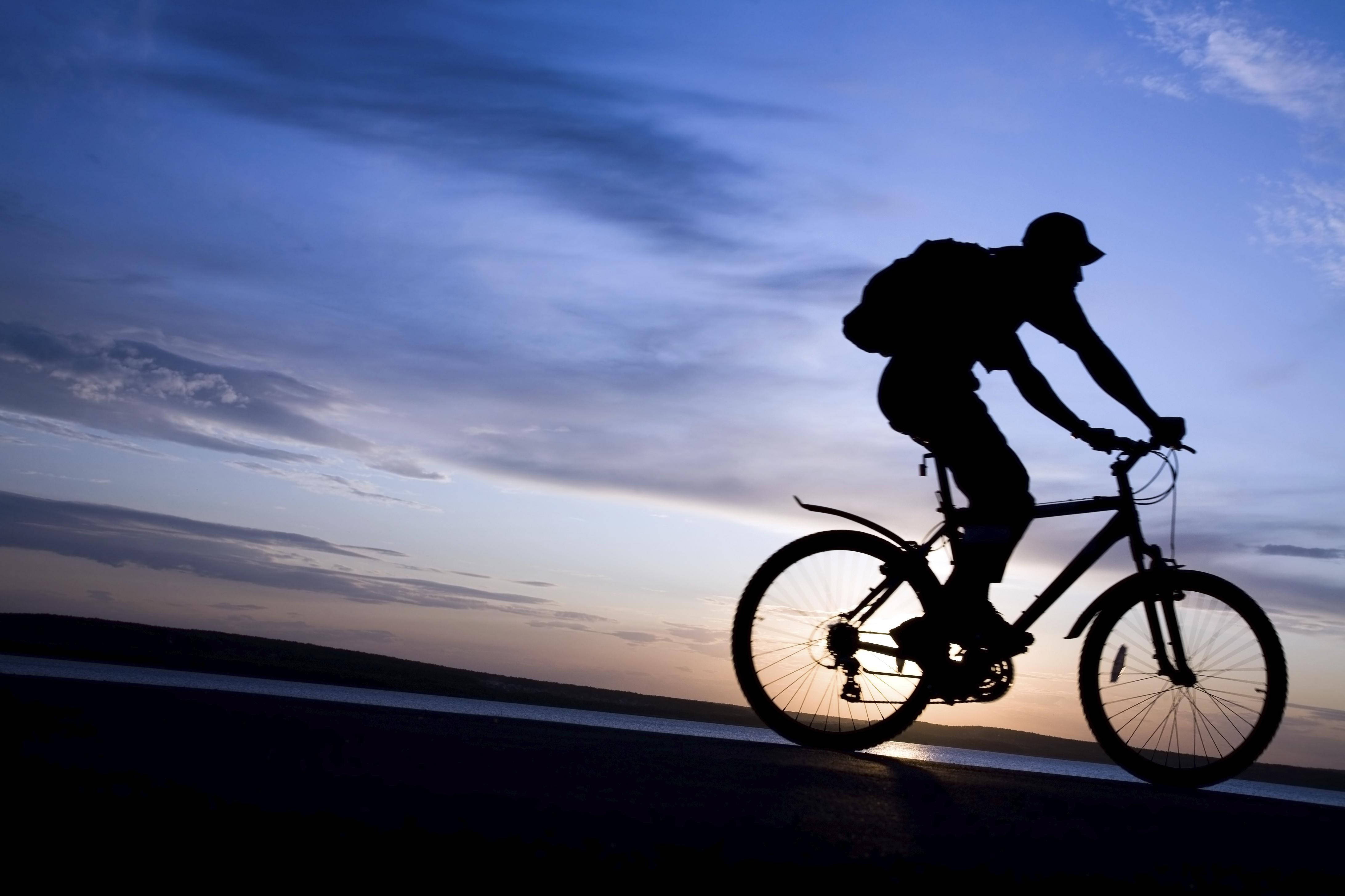 bike riding 桌布 壁紙 — 在暮色中，一名背著背包的騎車者在道路上騎單車，背景是漸變天空的剪影。
