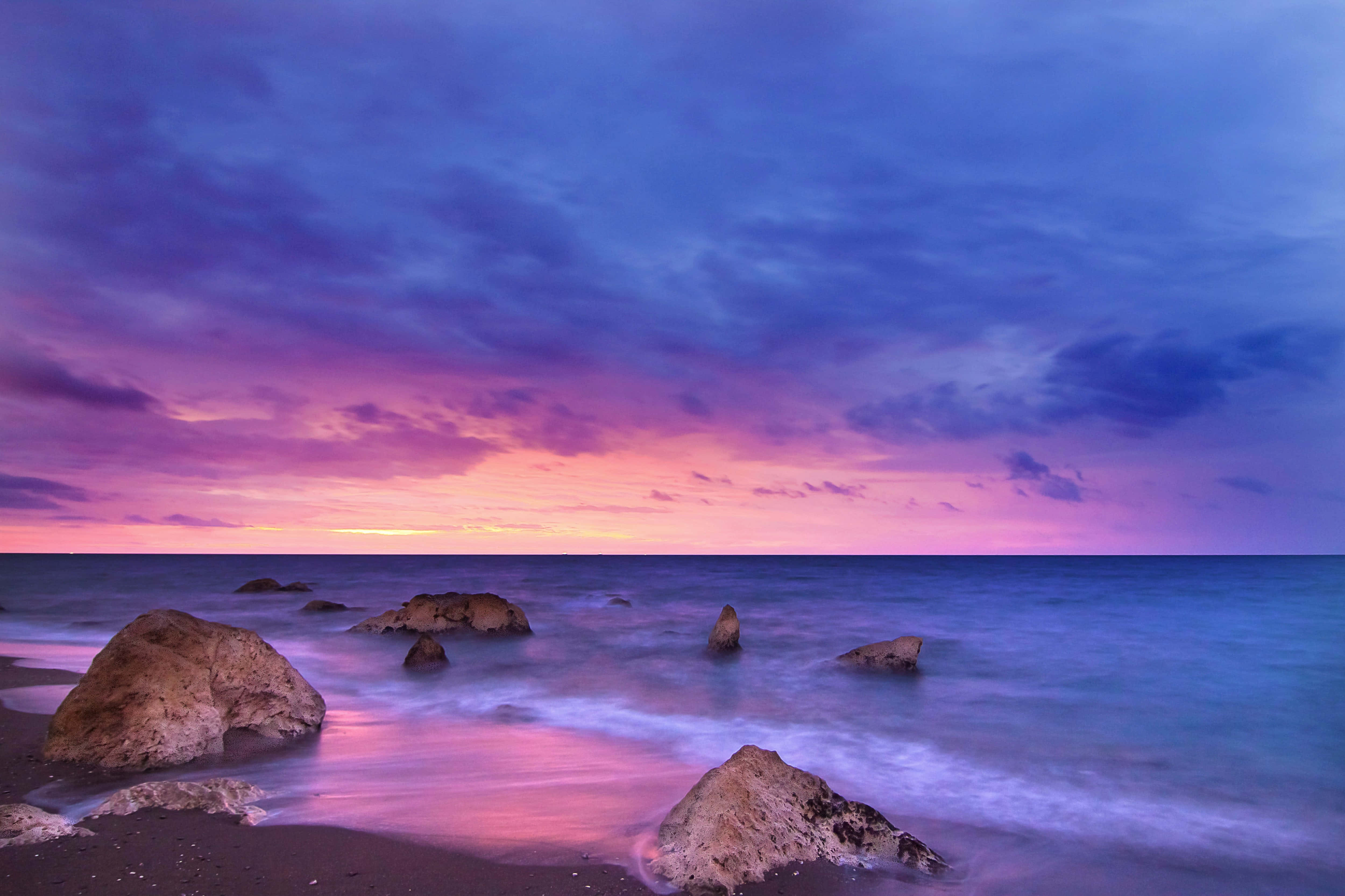 Pink Beach Sunset 桌布 壁紙 — 在暮色中長時間曝光的海景，平滑的水流繞過崎嶇的岩石，天空呈現鮮豔的紫色和粉紅色。