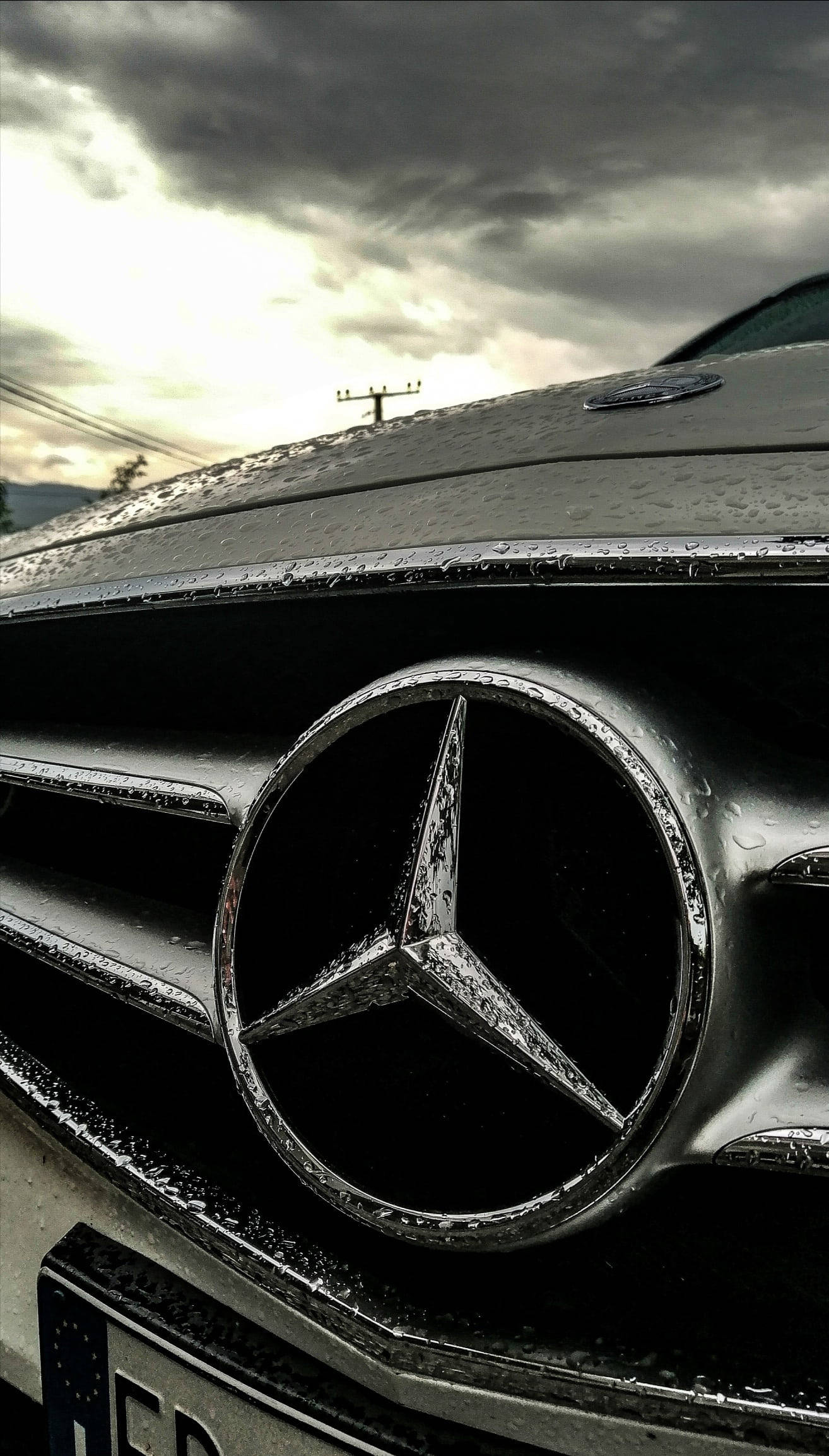 mercedes amg iPhone 桌布 壁紙 — 在暴風雨天空下，戲劇性燈光中，濕透的 Mercedes-Benz 水箱護罩特寫。