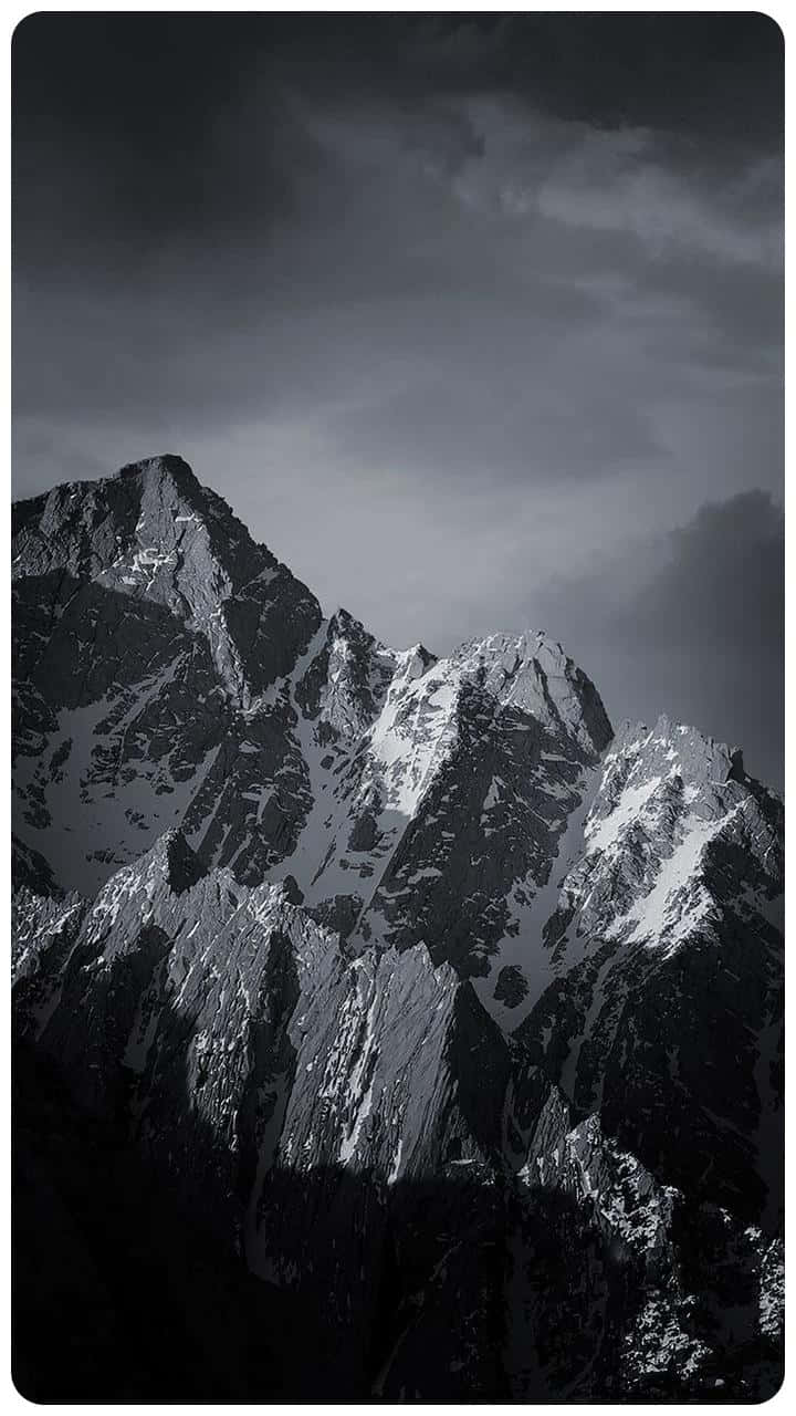 elegant 桌布 壁紙 — 在暴風雨的天空下，一個戲劇性的單色山峰，帶有積雪的山脊。