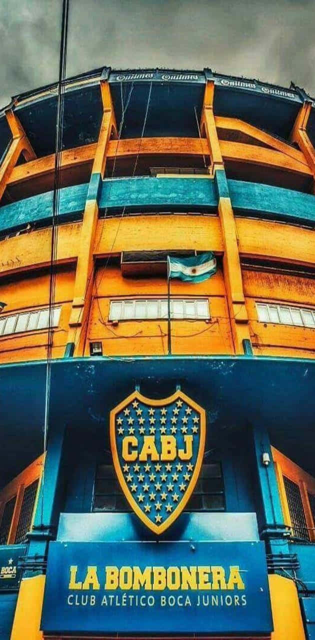 Stadium 桌布 壁紙 — 在暴風雨的天空下，以低角度觀看拉邦博內拉體育場標誌性的藍黃色外牆。