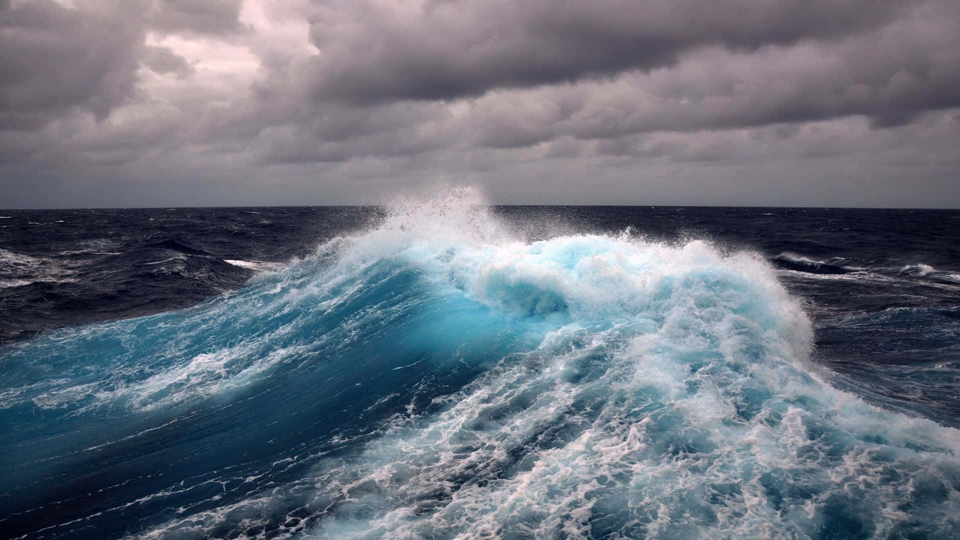 waves 桌布 壁紙 — 在暴風雨的海洋中，巨大的藍綠色波浪在沉重的灰色天空下破碎。