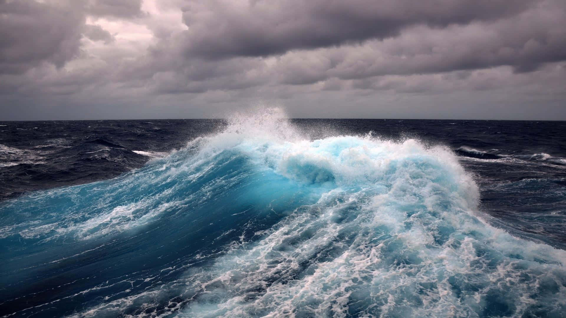 Ocean Waves 桌布 壁紙 — 在暴風雨的海洋中，巨大的藍綠色波浪在沉重的灰色天空下破碎。