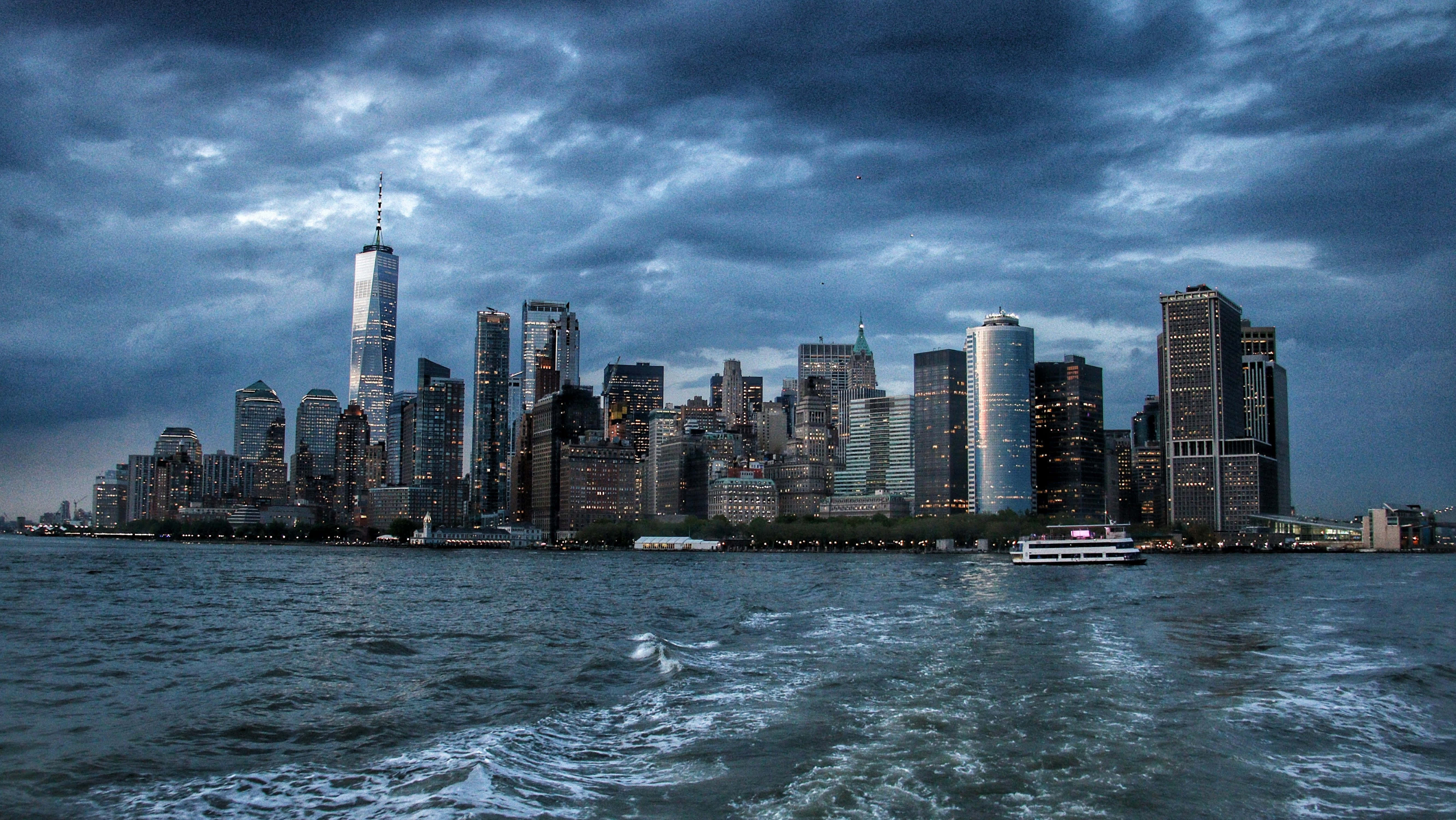 Nyc 桌布 壁紙 — 在暴風雲下，紐約市天際線的戲劇性暮色景觀，明亮的摩天大樓倒映在黑暗的水面上。