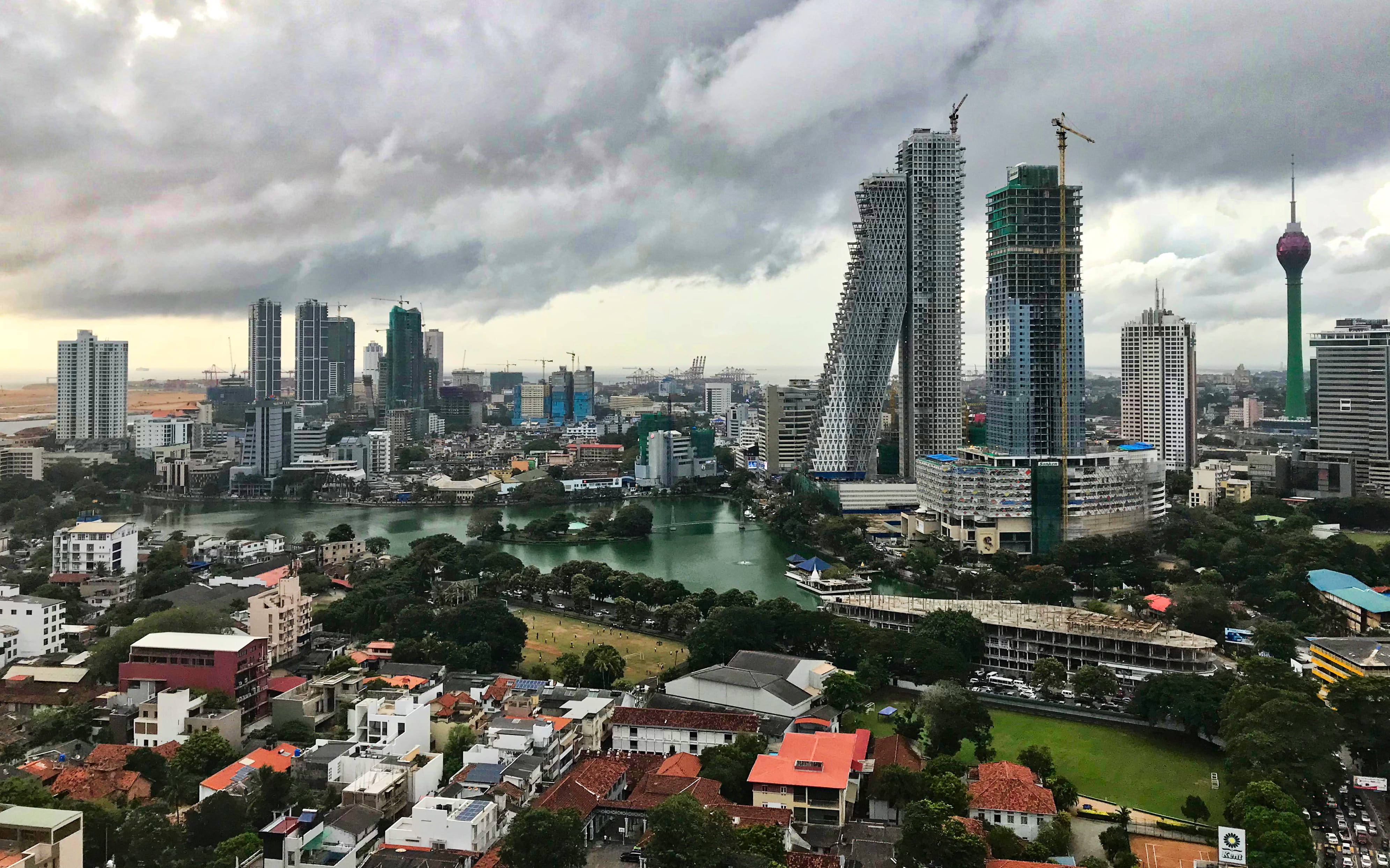 Sri Lanka 桌布 壁紙 — 在暴風雲下戲劇性的城市天際線，河流蜿蜒穿過密集的住宅區和現代高層建築。