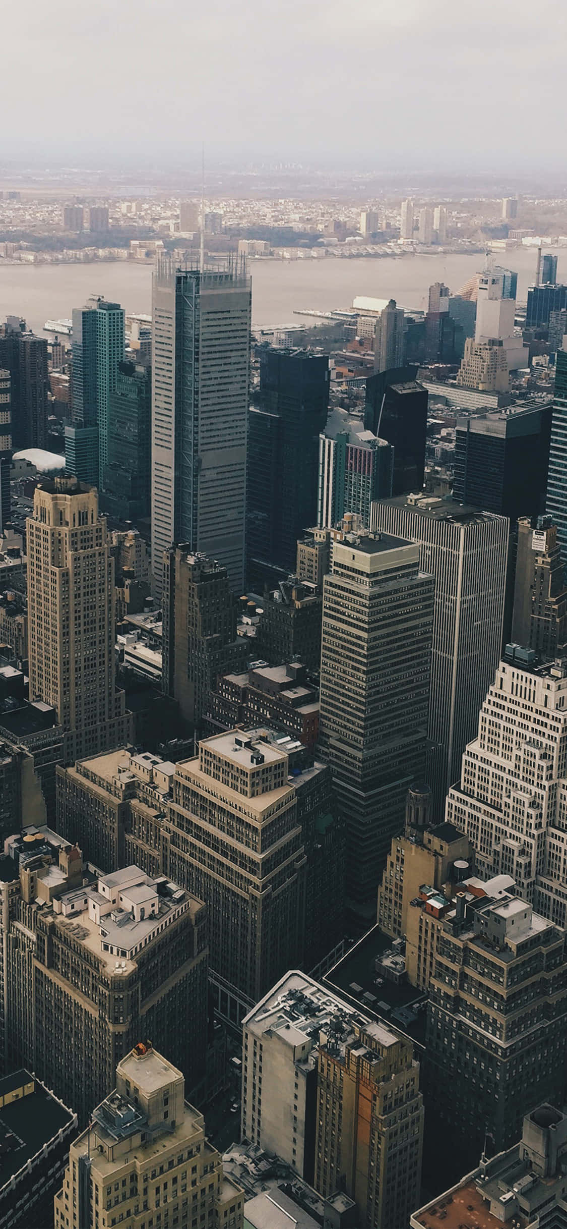 New York 桌布 壁紙 — 在朦朧天空下，廣闊大都市中密集的摩天大樓與遠處一條寬闊河流的航拍景觀。