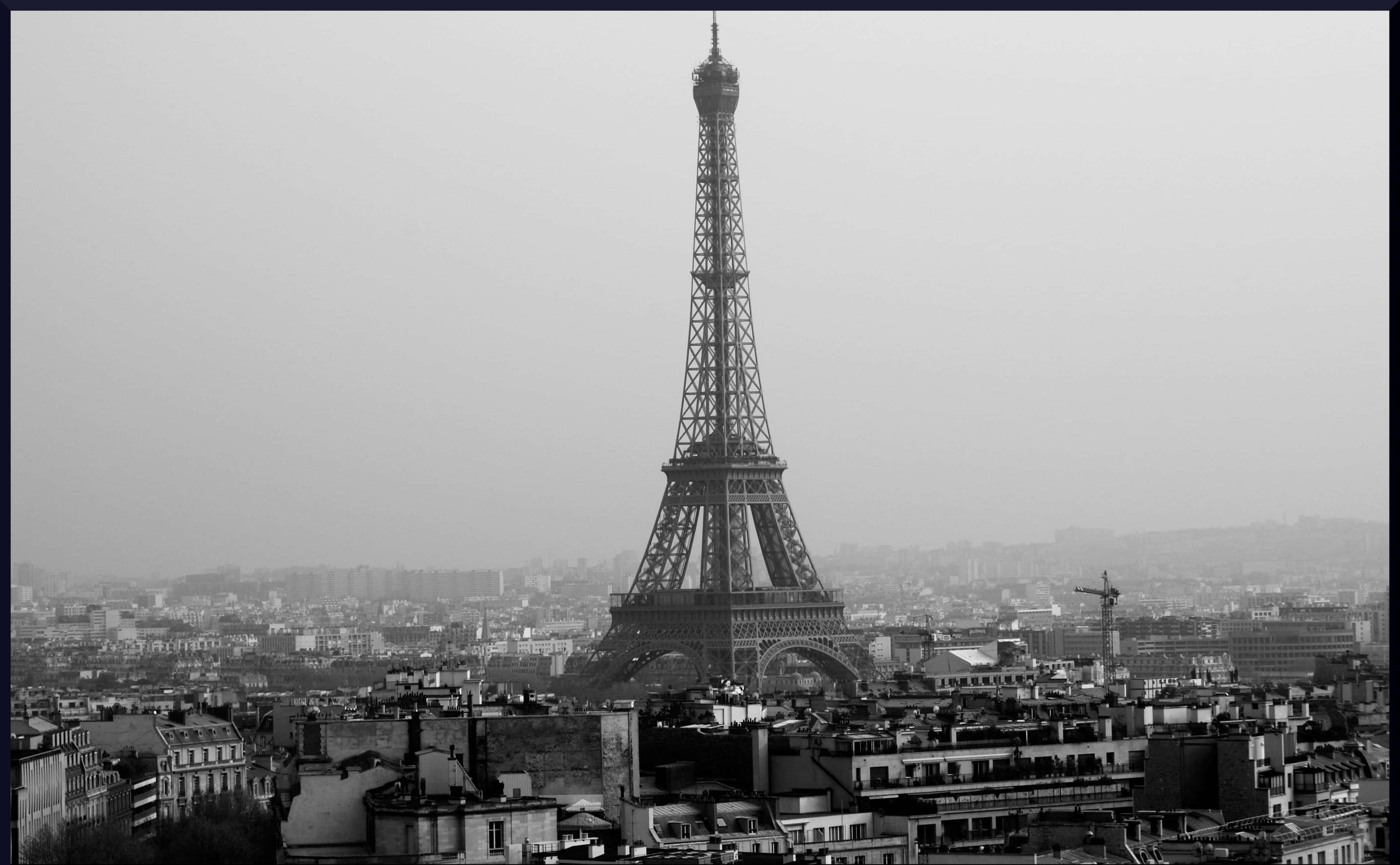 Black And White Cityscape 桌布 壁紙 — 在朦朧天空下，艾菲爾鐵塔從巴黎屋頂上方升起的單色景觀。