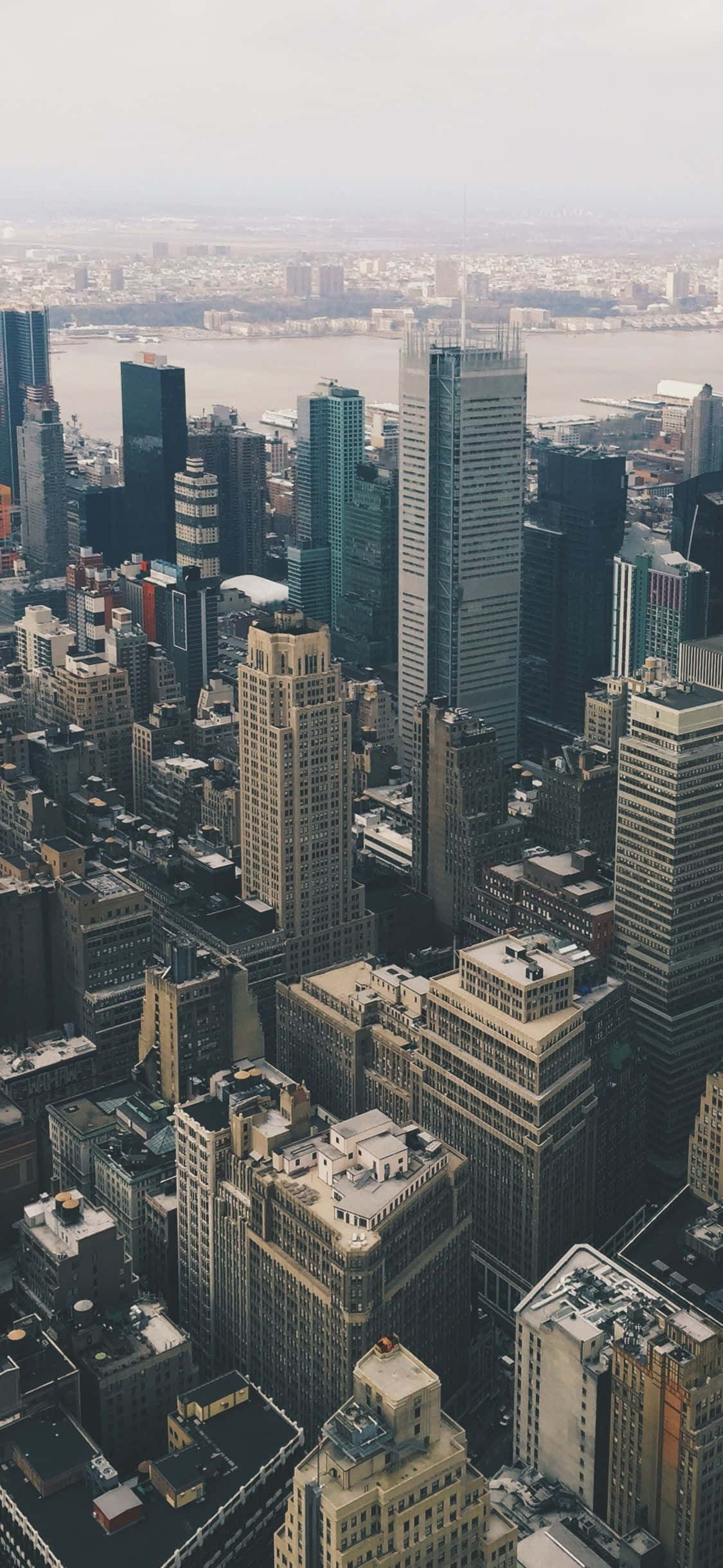 New York 桌布 壁紙 — 在朦朧日光下，密集城市天際線的高空景觀，有高聳摩天大樓和遠處的寬闊河流。