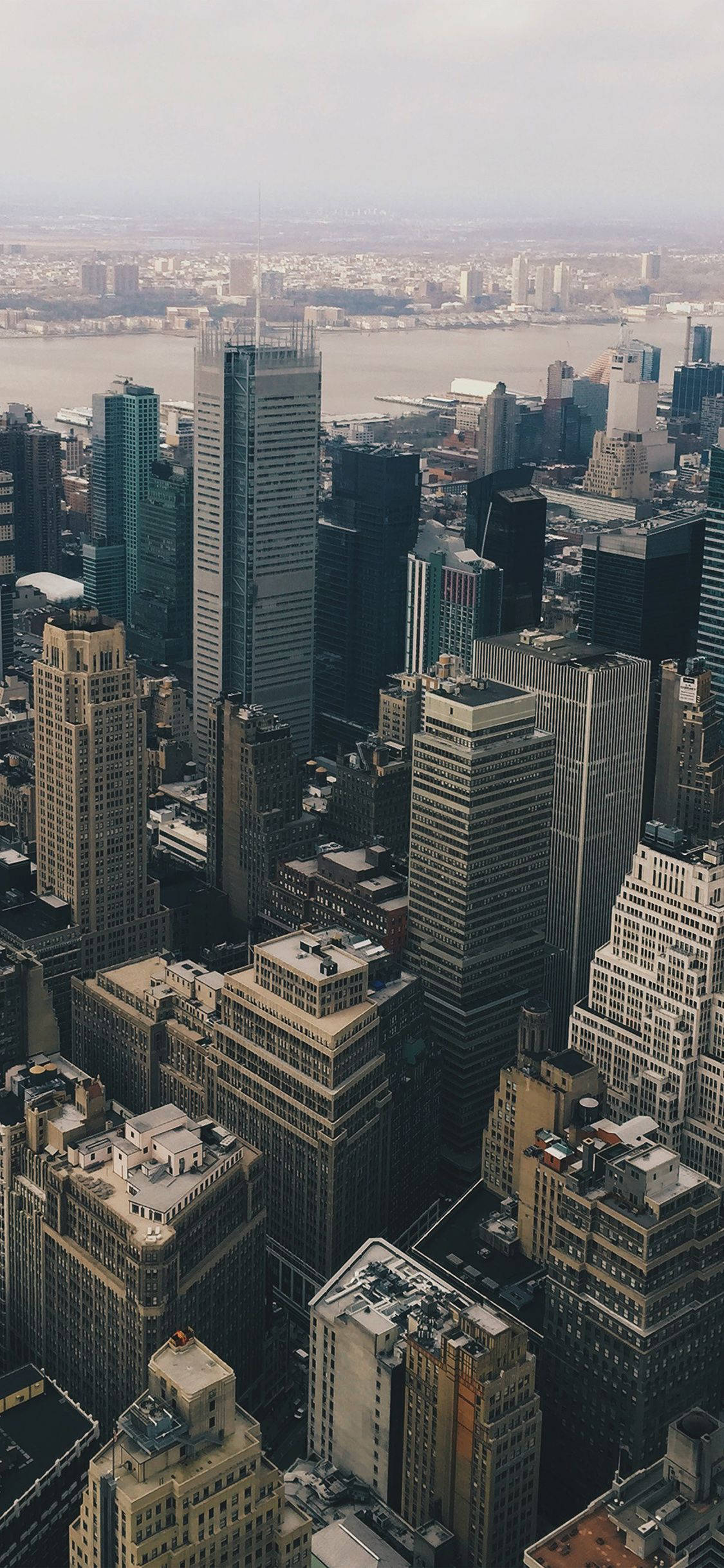 Skyscraper 桌布 壁紙 — 在朦朧日光下，廣闊大都市中密集摩天大樓的航拍視圖，遠處有一條寬闊的河流。