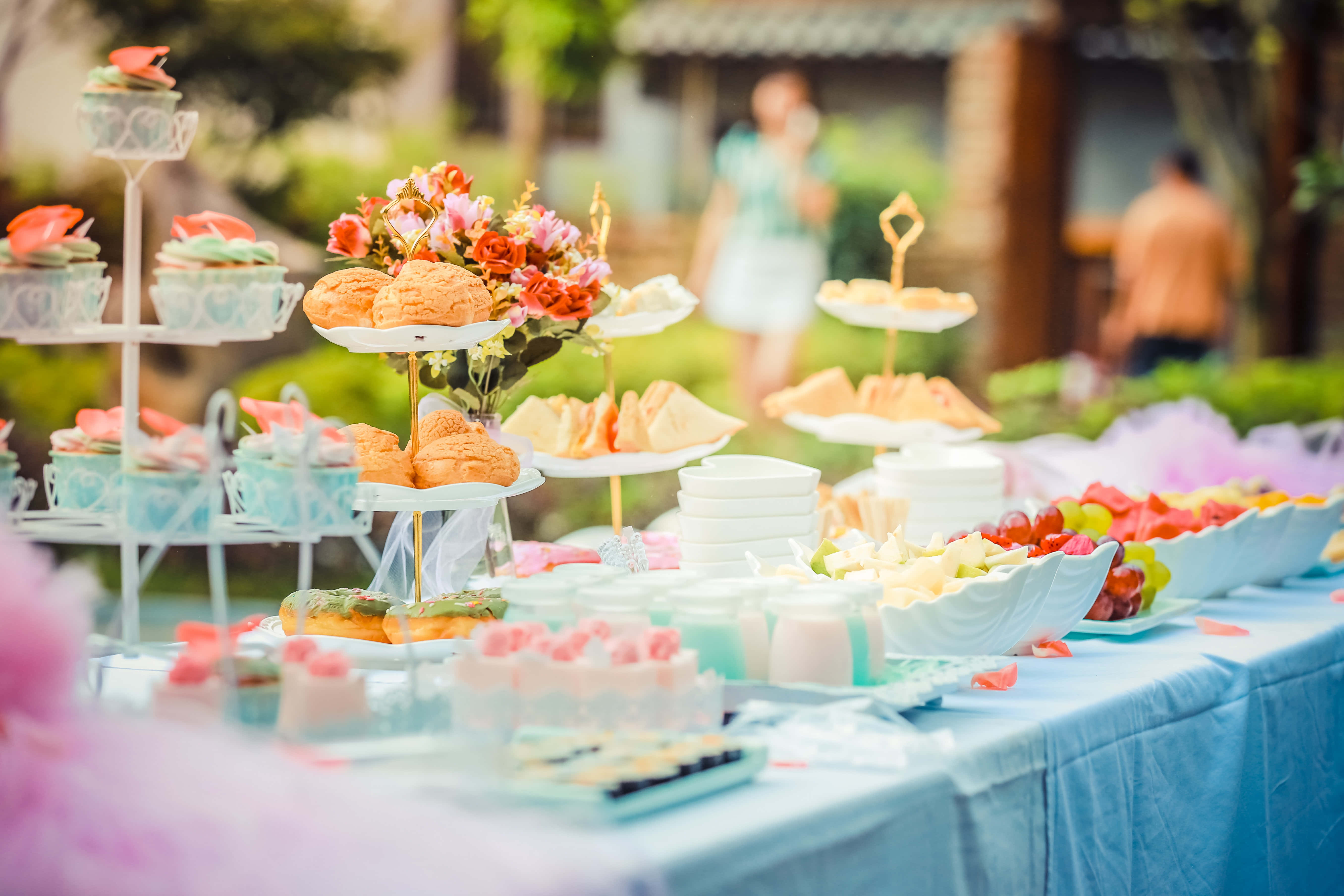 Baby Shower 桌布 壁紙 — 在柔和日光下，藍色桌布上擺滿了粉彩甜點、鮮花和水果的豪華戶外茶會。