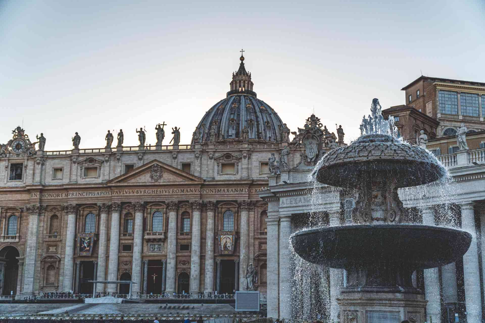 Rome 桌布 壁紙 — 在柔和暮色天空下，一座宏偉的巴洛克噴泉在聖彼得大教堂及其標誌性圓頂前噴水。