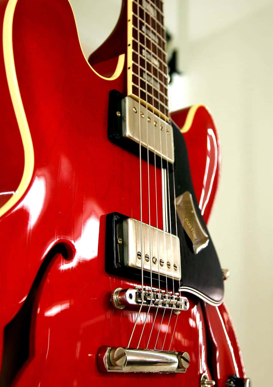 Guitar Aesthetic 桌布 壁紙 — 在柔和白色背景上，帶有金色飾邊和鍍鉻硬體的亮紅色電吉他的特寫。