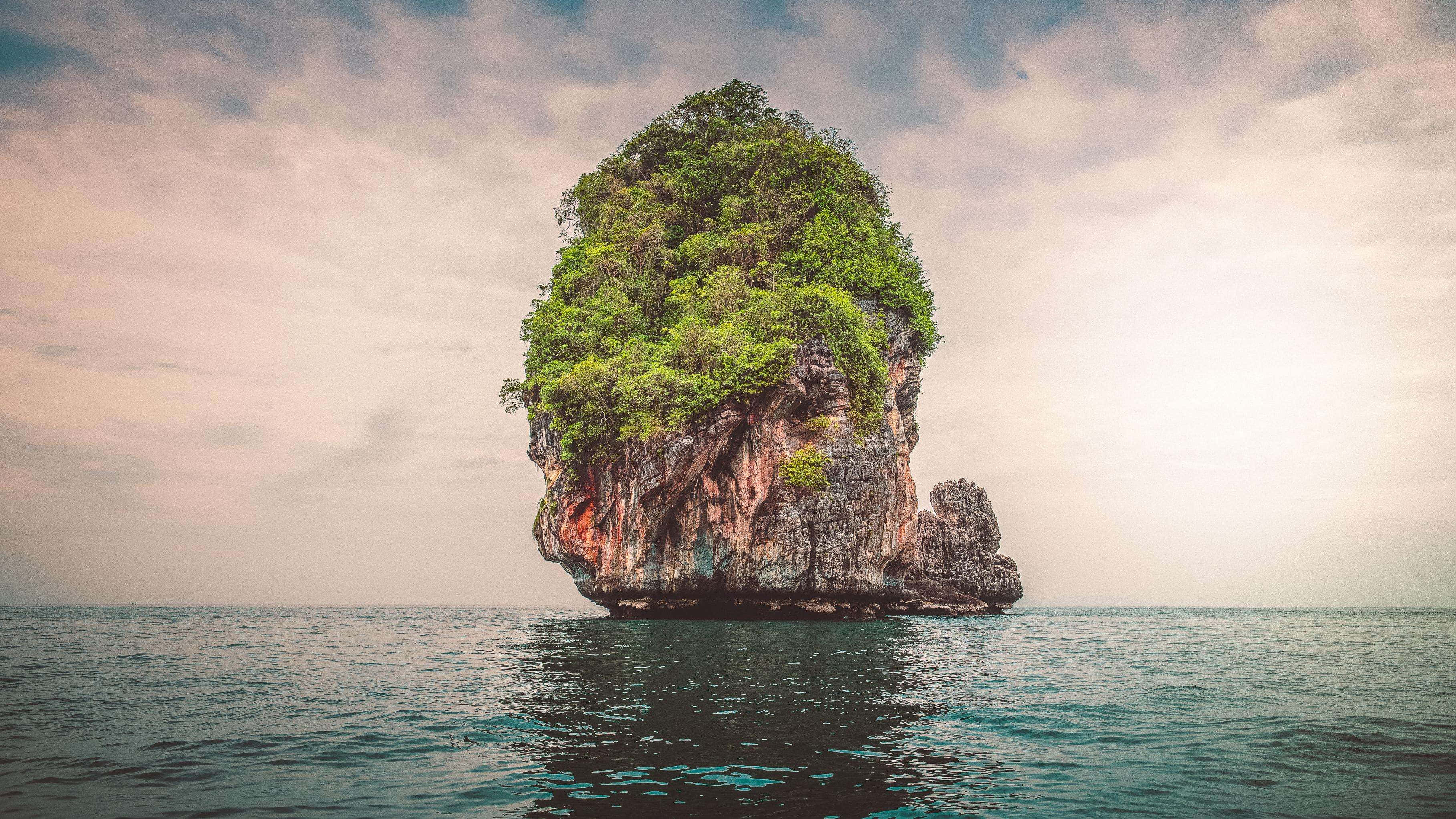 泰國 桌布 壁紙 — 在柔和的多雲天空下，一個鬱鬱蔥蔥的綠色島嶼從平靜的海水中戲劇性地升起。