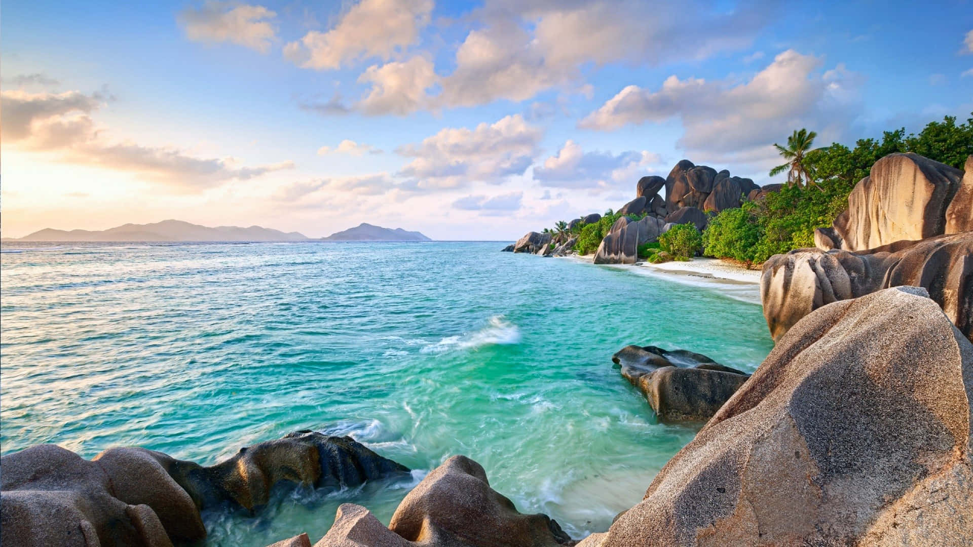 Hi Res Beach 桌布 壁紙 — 在柔和的金色日落天空下，碧綠的海水拍打著偏遠熱帶海灘上的巨大花崗岩巨石。
