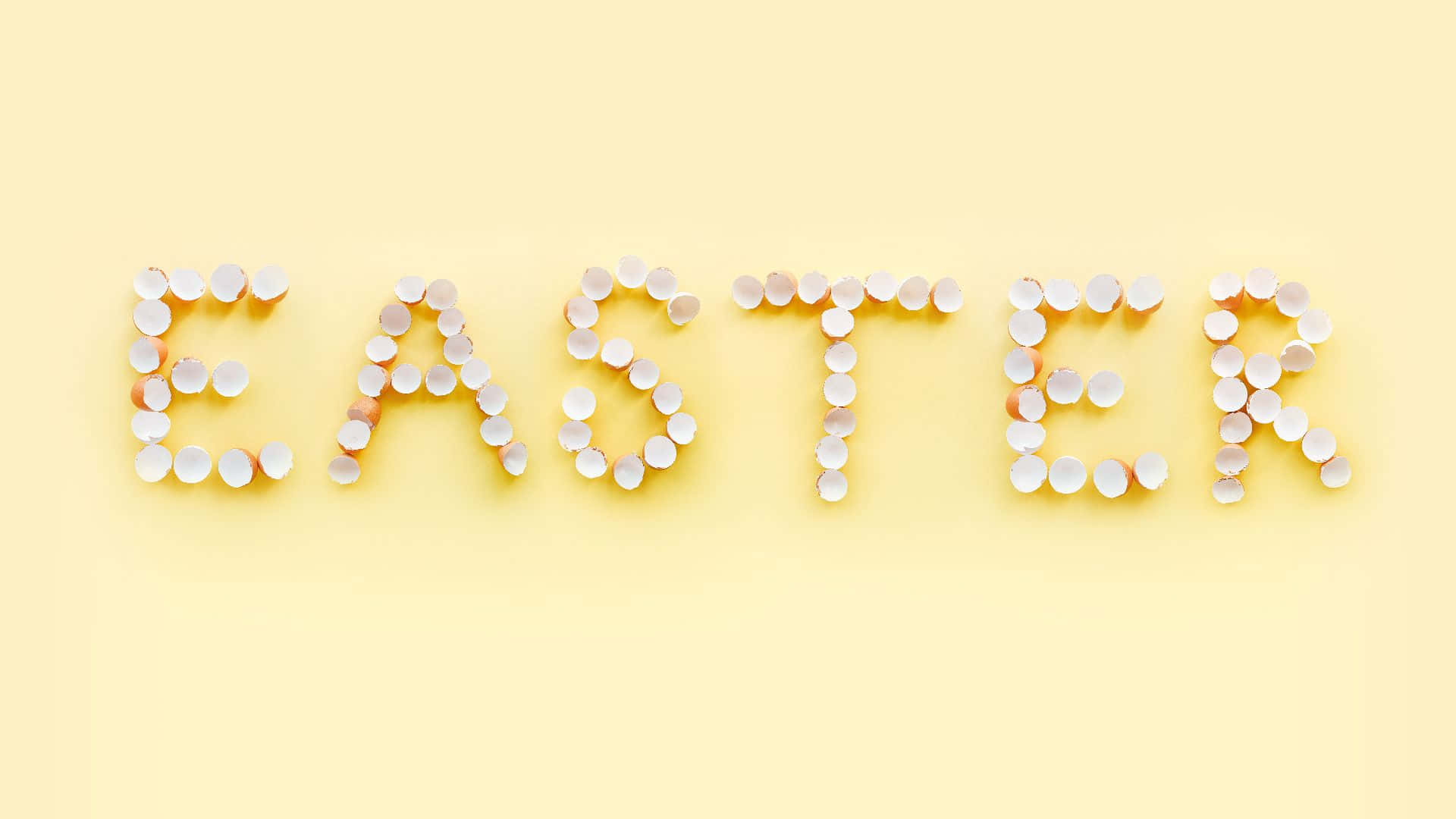 Easter Zoom 桌布 壁紙 — 在柔和的黃色背景上，用破碎的蛋殼半邊拼出「EASTER」這個詞。