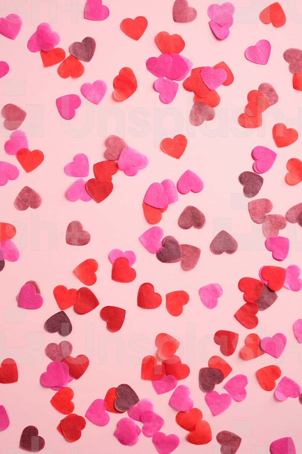 Heart Shape 桌布 壁紙 — 在柔軟的粉紅色背景上散落著紅色、粉紅色和酒紅色的氈製心形，以平鋪方式展示。
