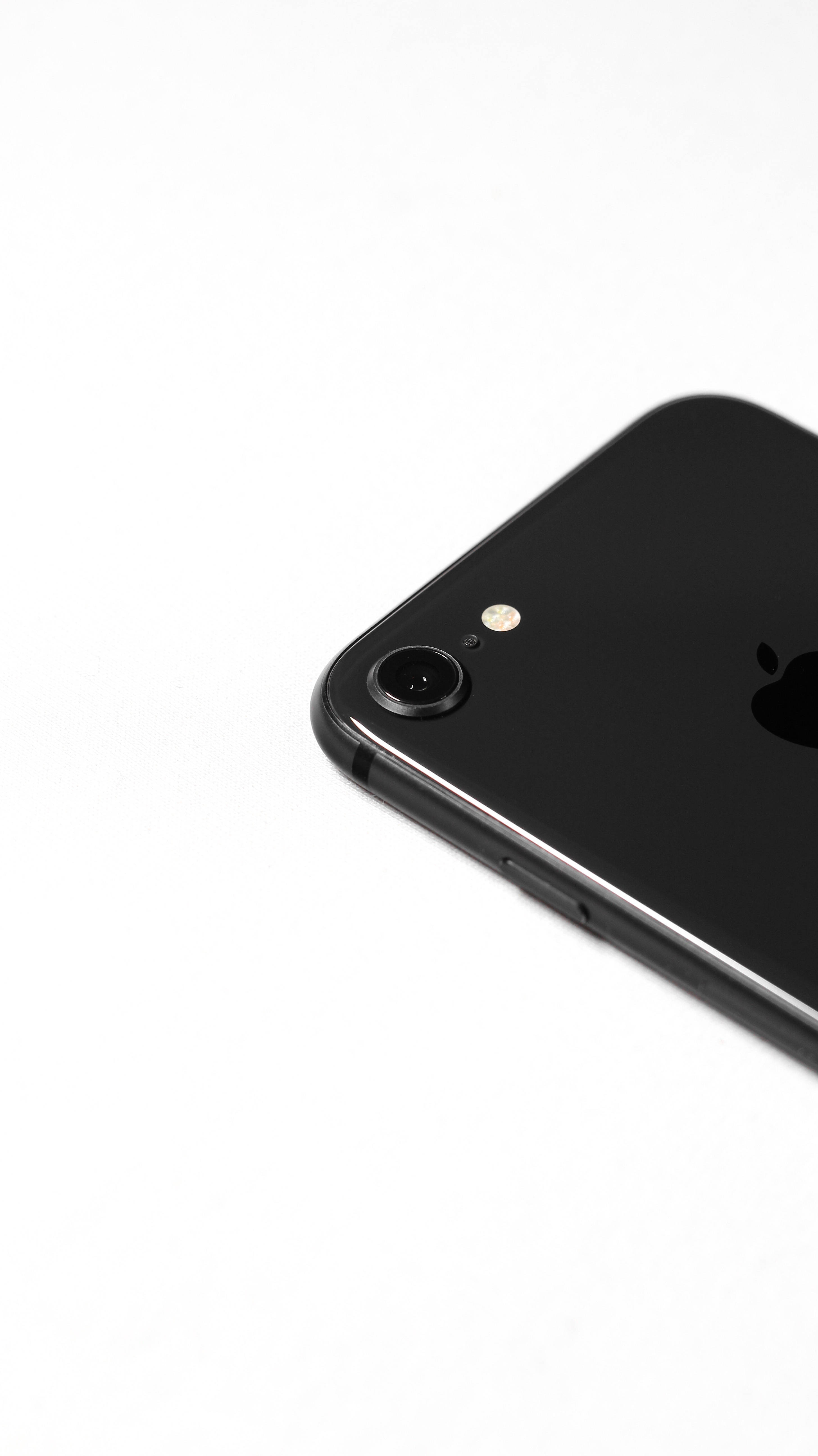 Dark Aesthetic iPhone 桌布 壁紙 — 在極簡白色背景上，黑色iPhone一角的特寫，突出其相機和標誌。