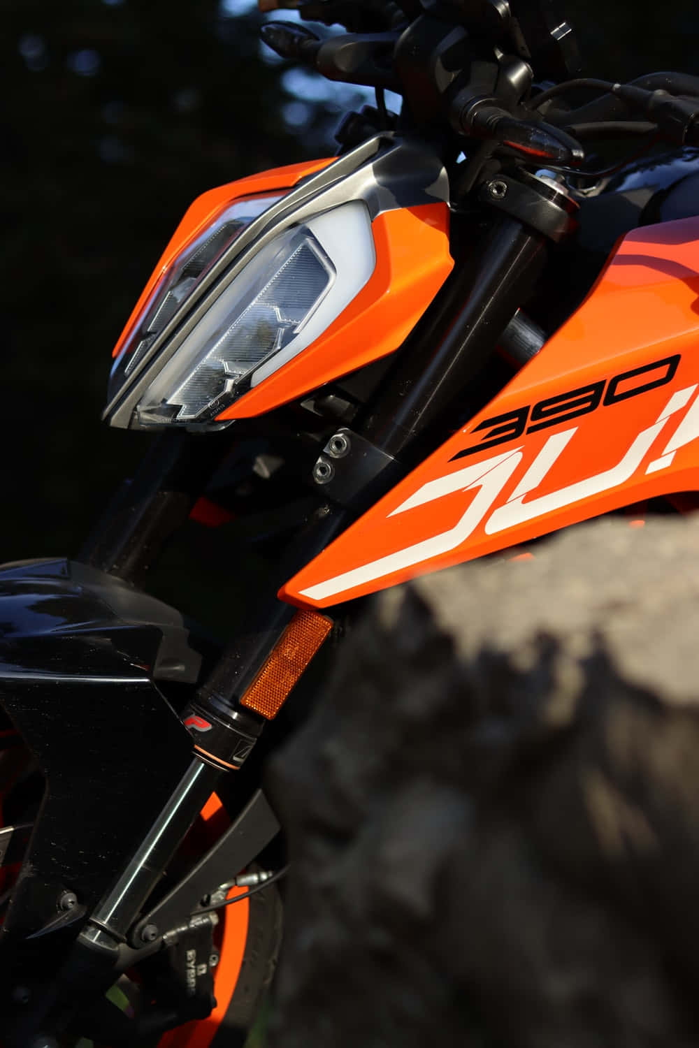 Duke 桌布 壁紙 — 在模糊岩石地形背景下，鮮橙色KTM 390 Duke摩托車頭燈和前整流罩的特寫。