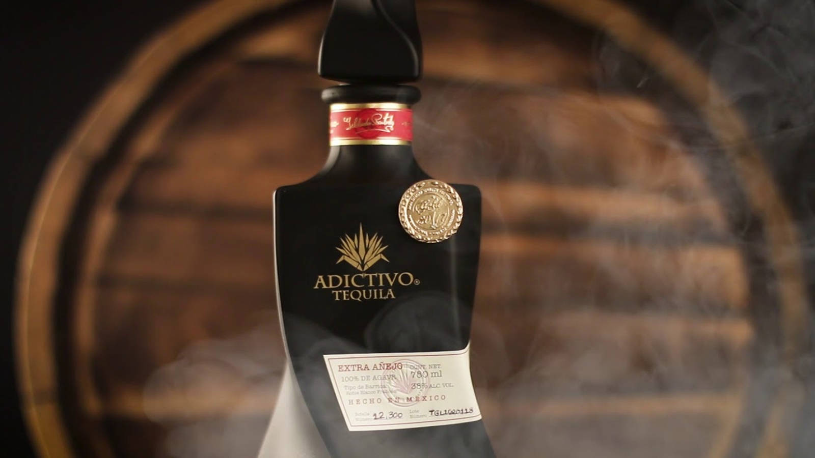 電腦 桌布 壁紙 — 在模糊的木桶背景下，一個時尚的黑色Adictivo Tequila Extra Añejo酒瓶散發著煙霧。
