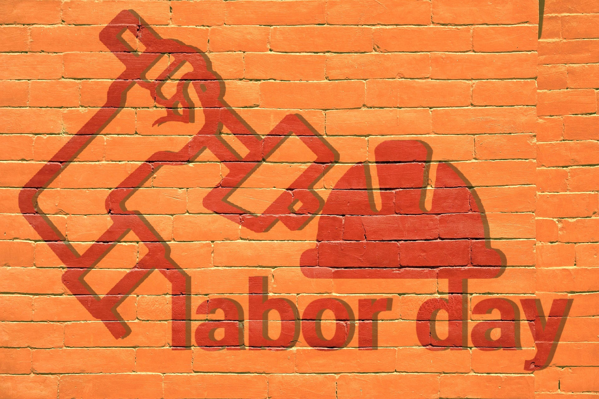 Labor 桌布 壁紙 — 在橙色磚牆上大膽的紅色塗鴉描繪了錘子和安全帽，並帶有labor day字樣。