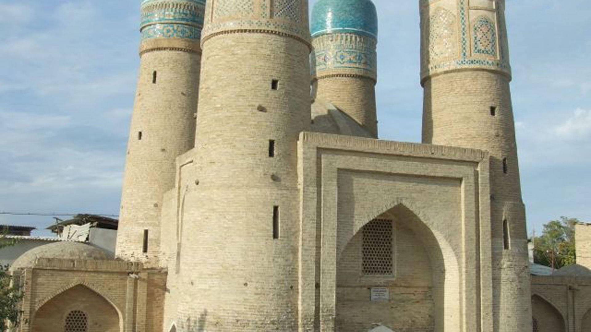 Uzbekistan 桌布 壁紙 — 在歷史伊斯蘭建築群中，古老的磚造宣禮塔與綠松石瓷磚圓頂在部分多雲的天空下聳立。