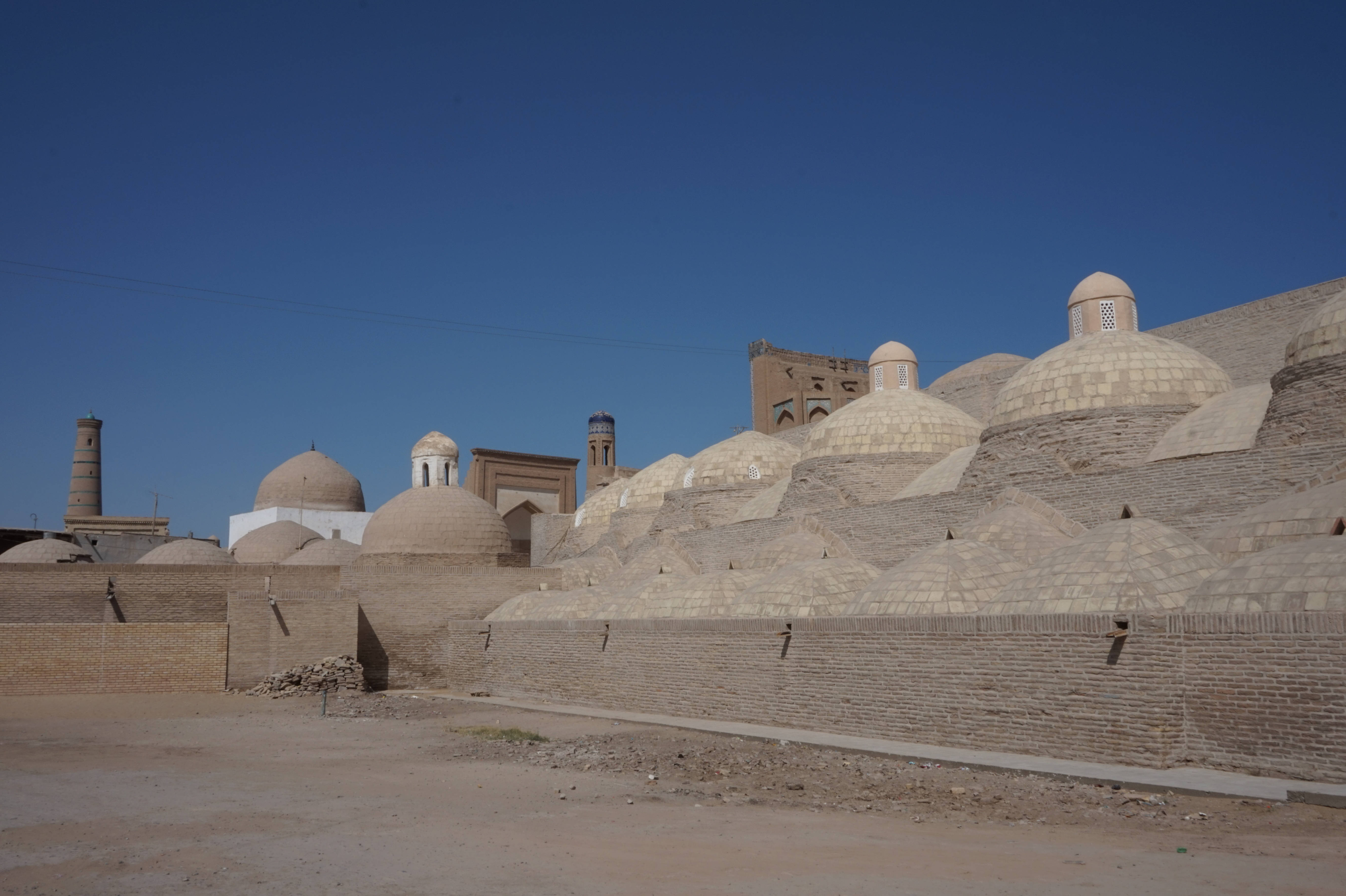 Uzbekistan 桌布 壁紙 — 在歷史悠久的伊斯蘭建築群中，古老的圓頂建築和宣禮塔從乾旱的土地上聳立，映襯著清澈的藍天。