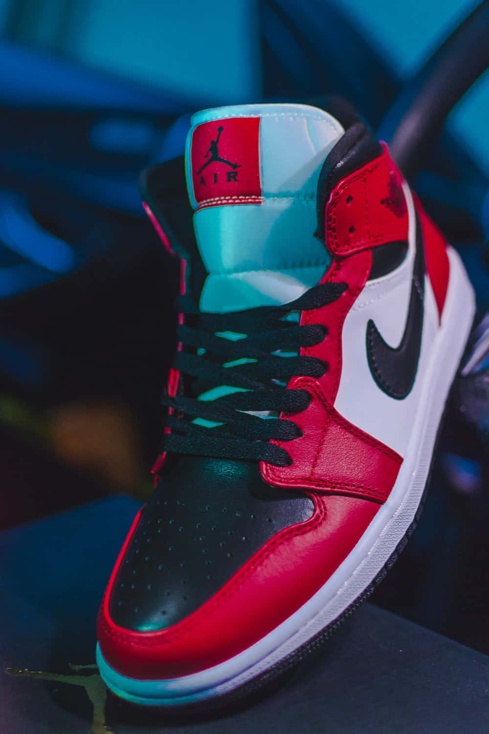 邁克爾·喬丹 桌布 壁紙 — 在氣氛藍色燈光下，紅、黑、白色Jordan 1運動鞋的特寫，帶有青綠色點綴。