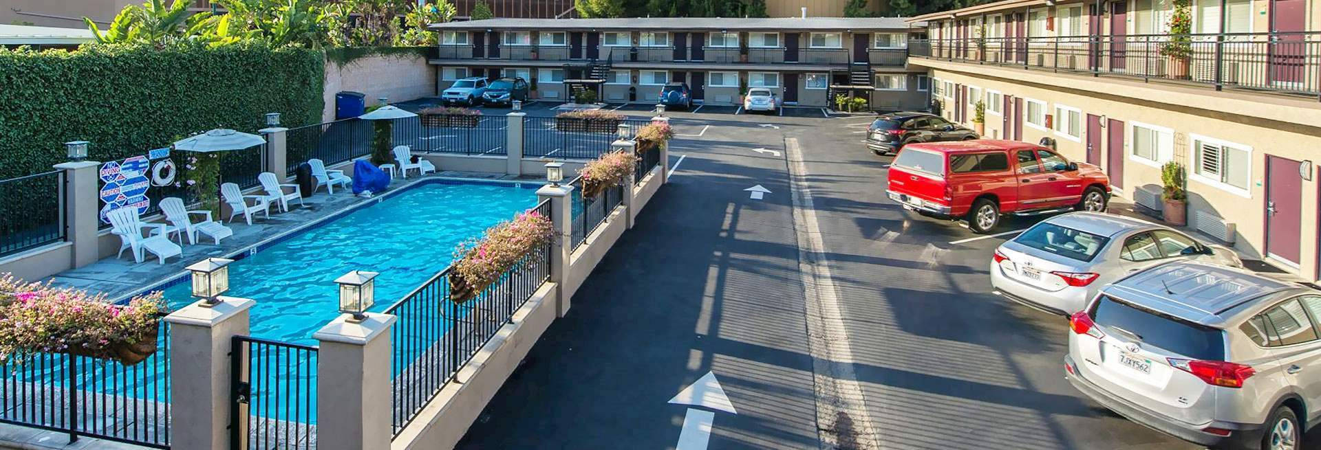 Hotel 桌布 壁紙 — 在汽車旅館的一個晴朗日子，有一個清澈的藍色游泳池，周圍環繞著白色躺椅和停泊的汽車。