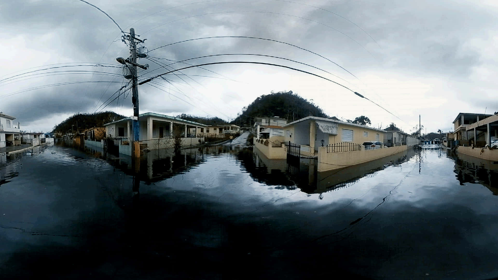 Flood 桌布 壁紙 — 在沉重的灰色天空下，被淹沒的街道上有被水淹沒的房屋和電線。