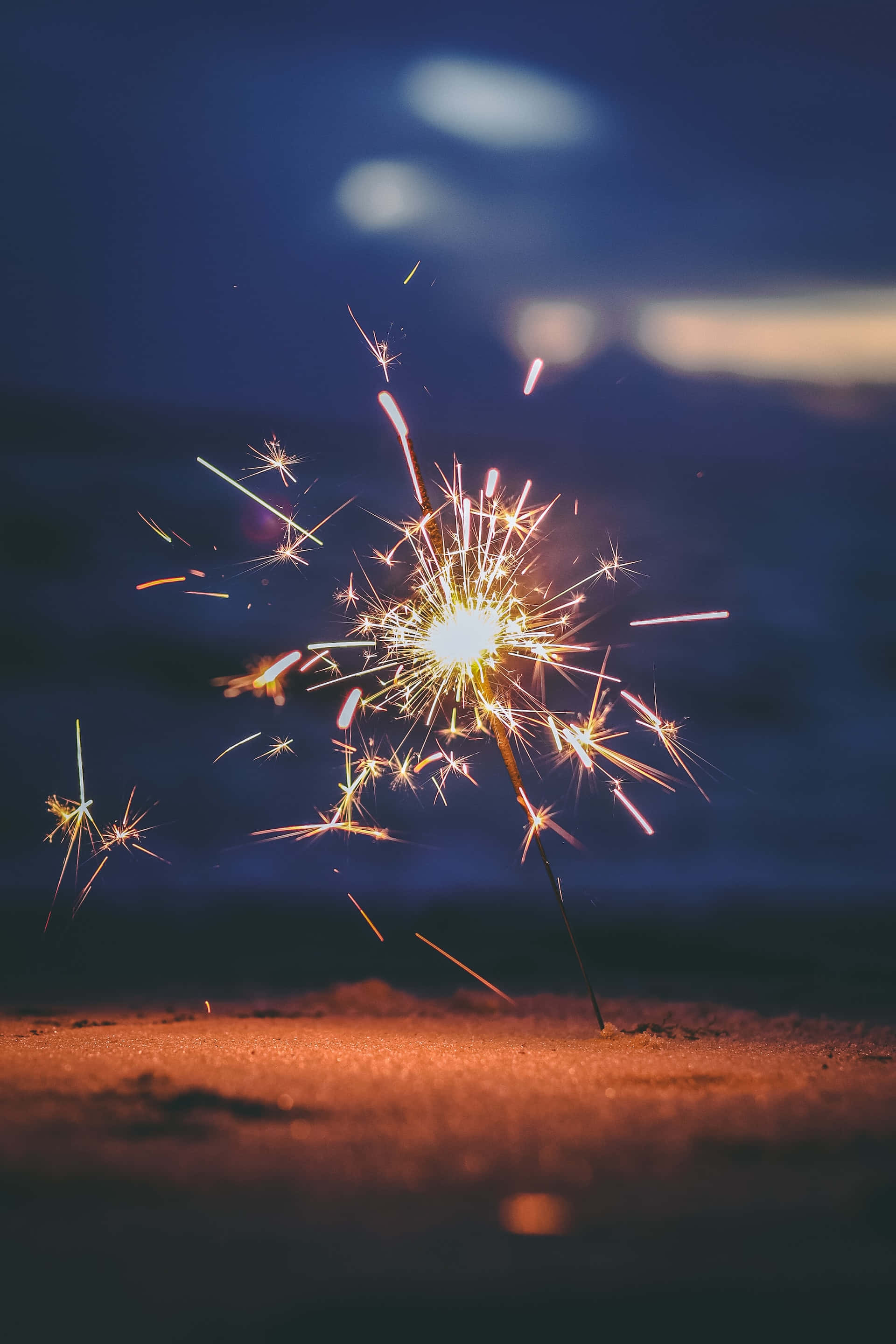sparks 桌布 壁紙 — 在沙地上空的深藍色暮色天空中，閃爍的煙火綻放出金色光芒。