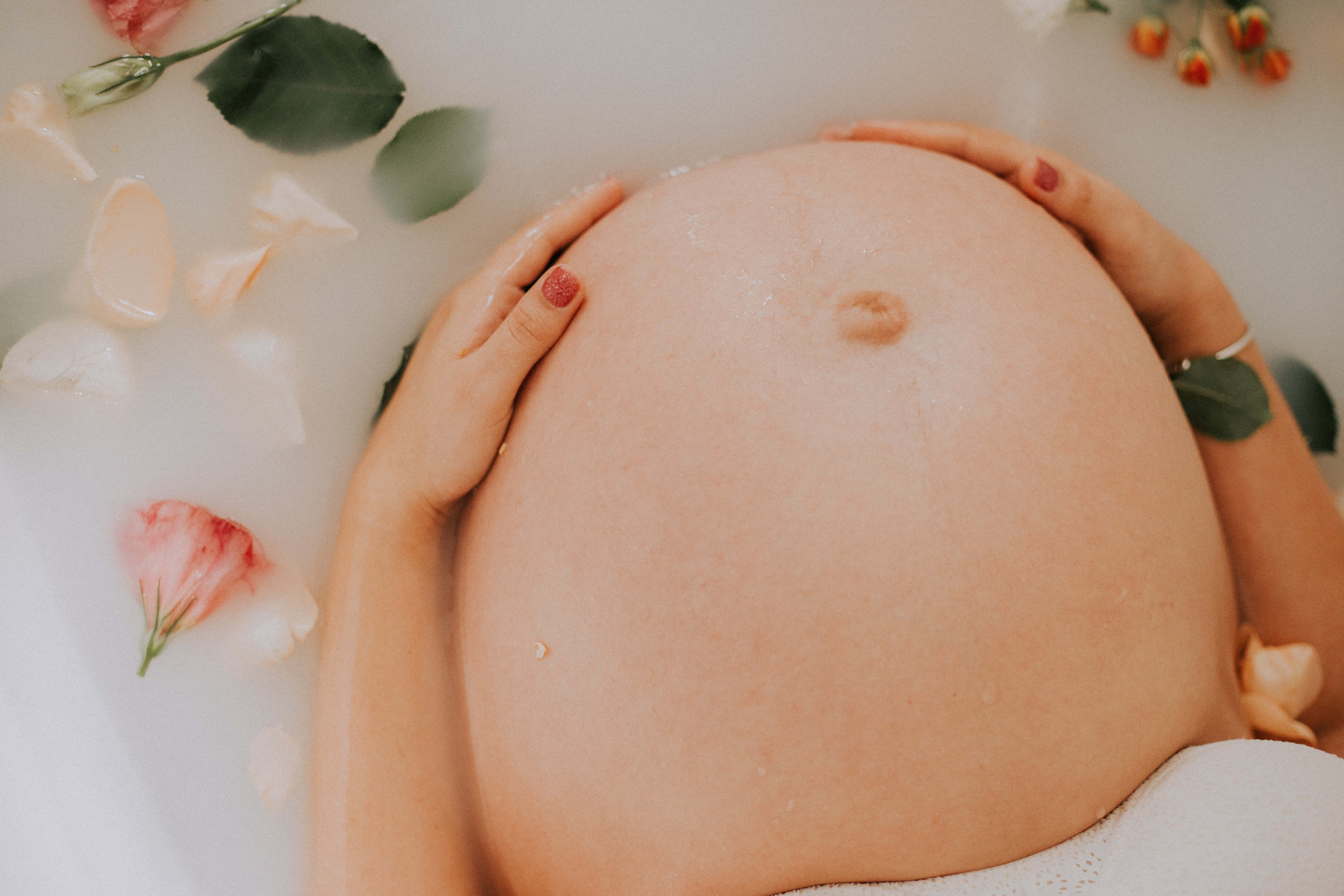 Pregnant 桌布 壁紙 — 在浴缸中，雙手捧著孕肚，周圍漂浮著玫瑰花瓣和綠葉。