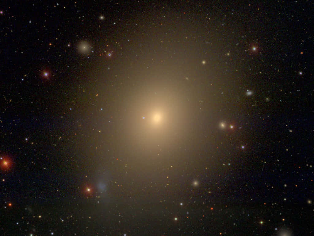 Elliptical Galaxy 桌布 壁紙 — 在深空中，一個明亮的螺旋星系在散佈著紅色和白色星星的星場中溫暖地發光。