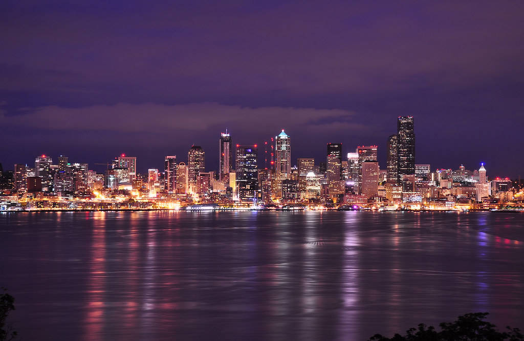 Seattle Skyline 桌布 壁紙 — 在深紫色天空下，閃爍的摩天大樓倒映在平靜水面上，充滿活力的城市夜景。