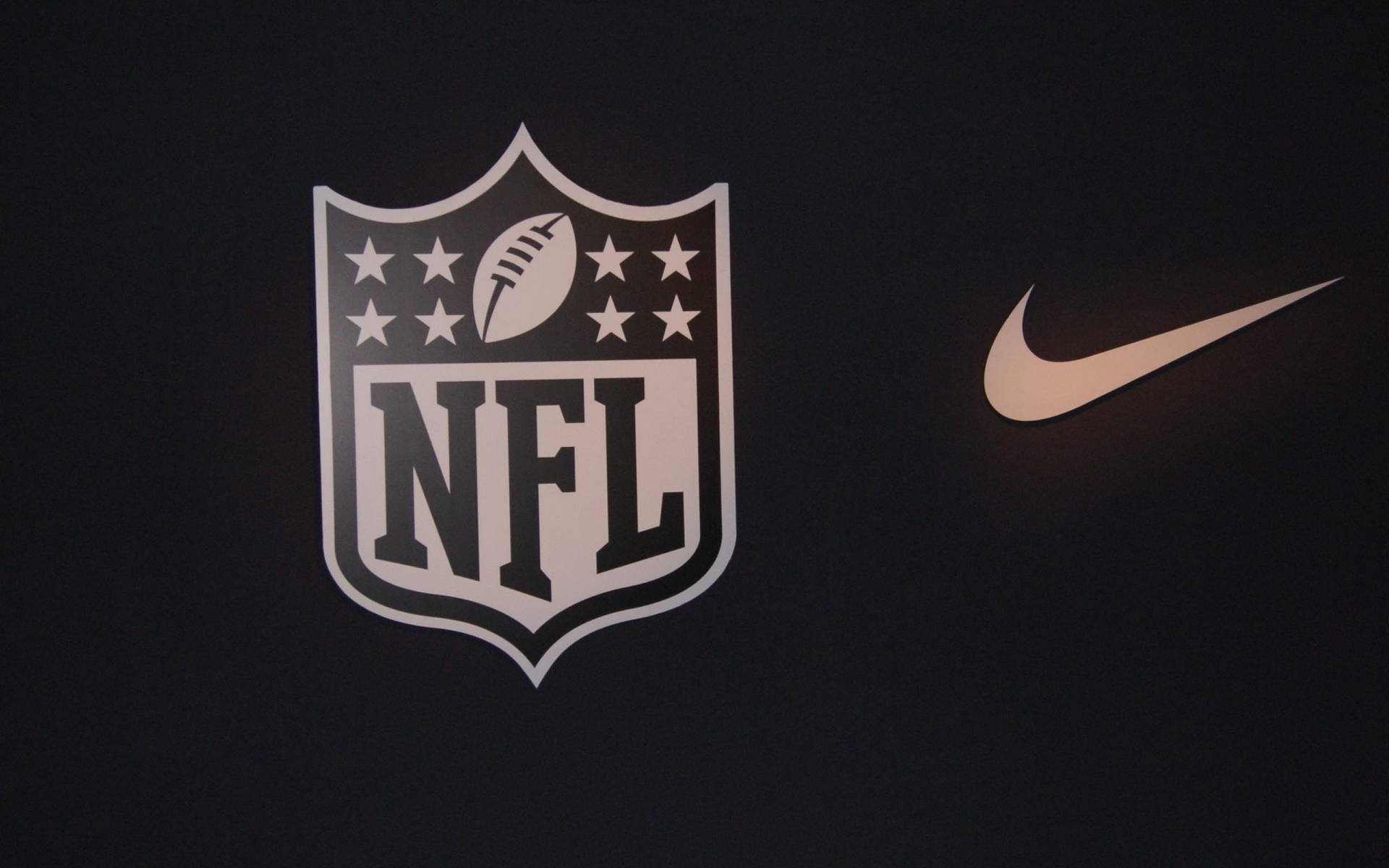 Nike 桌布 壁紙 — 在深色布料背景上，白色和金色的NFL盾牌標誌和Nike勾勾。