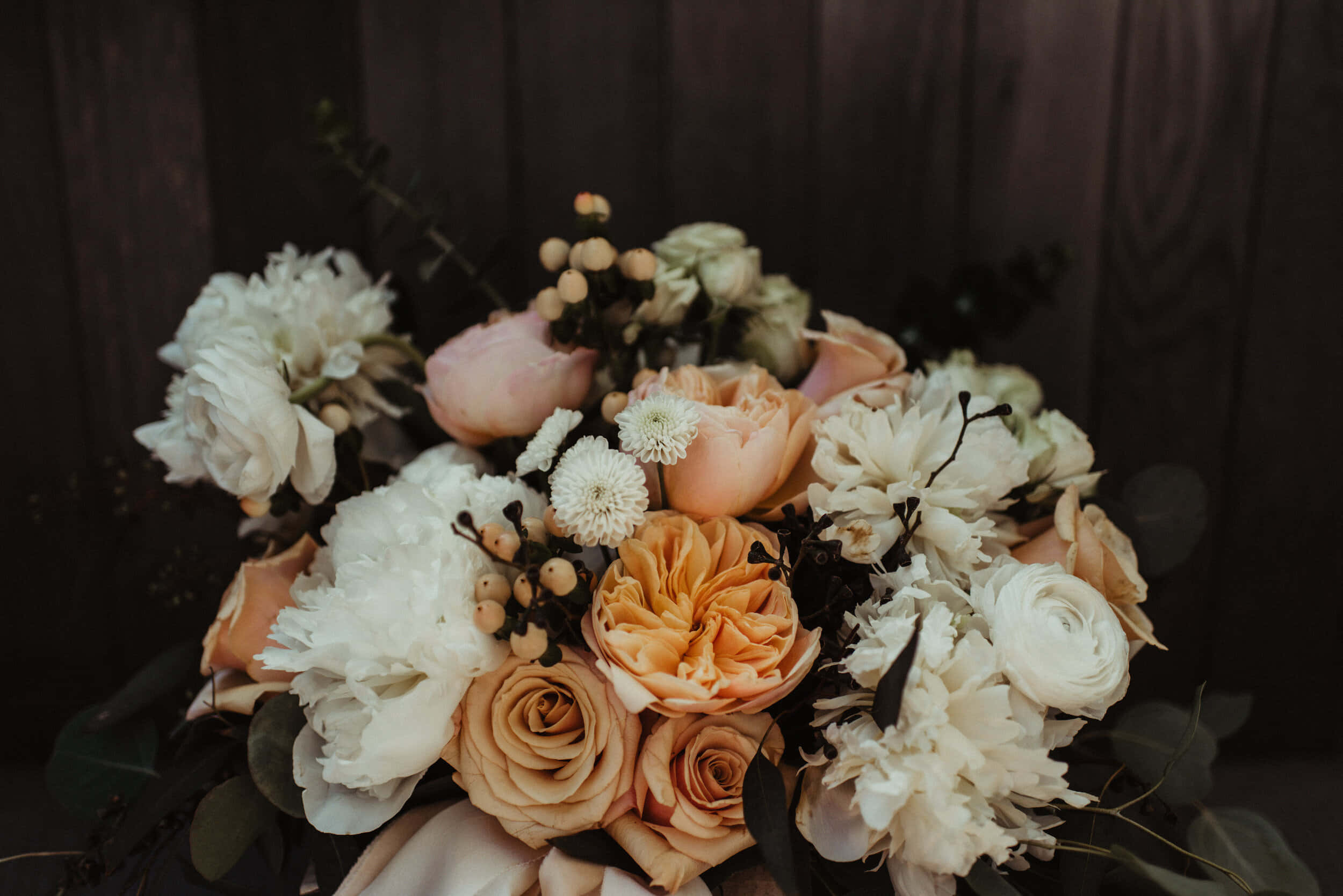 Wedding Bouquet 桌布 壁紙 — 在深色木質背景下，一束豐盛的蜜桃白和奶油色花朵，搭配漿果和綠葉。
