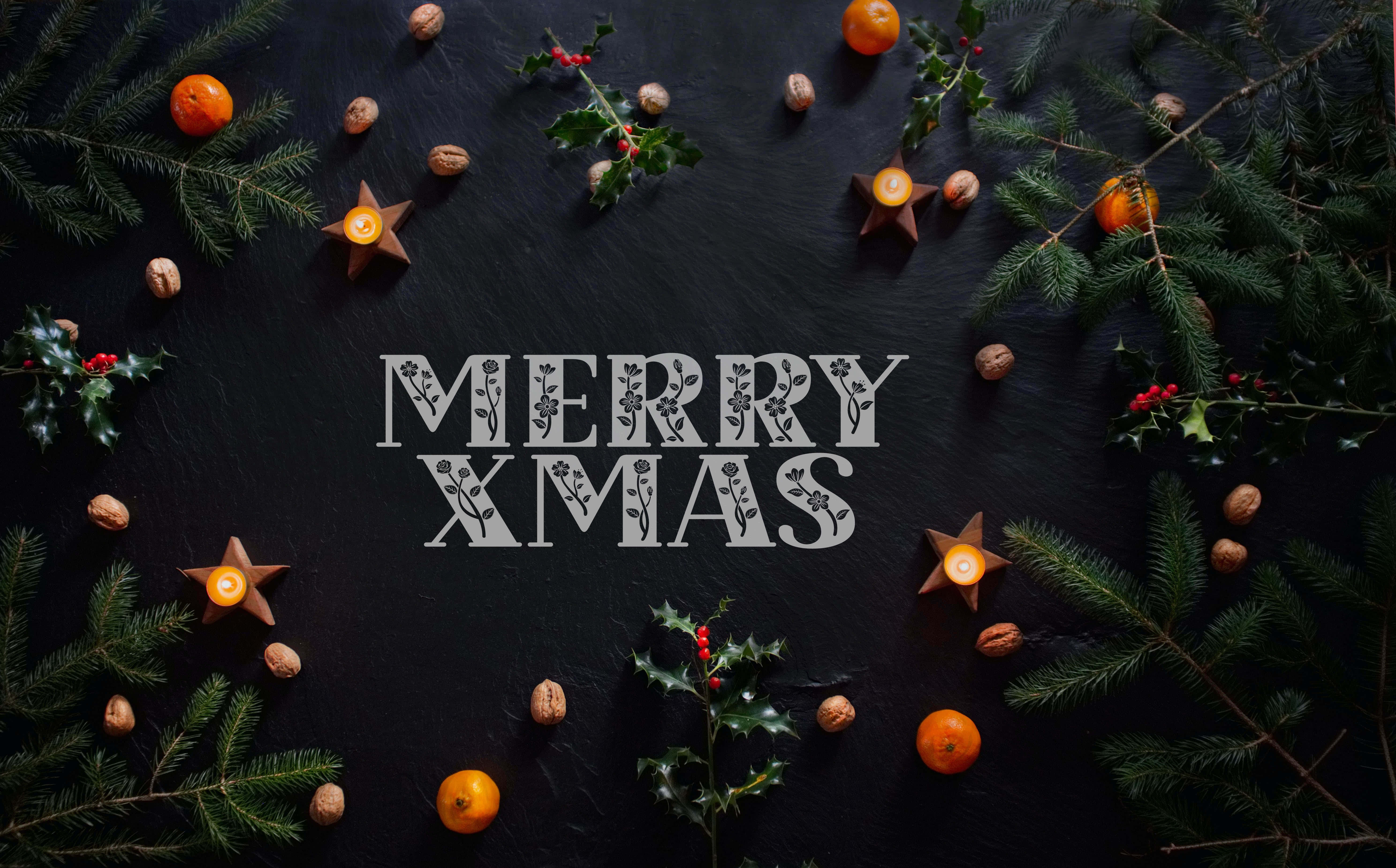 節日 桌布 壁紙 — 在深色石板背景上，裝飾字體的「Merry Xmas」文字被松樹枝、冬青漿果、橙子和點燃的星星蠟燭環繞。