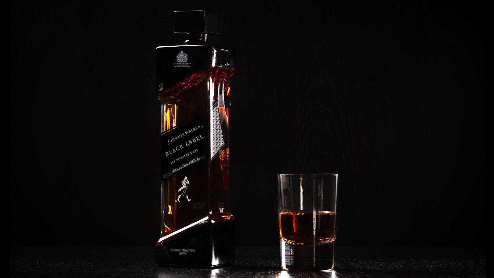 drinks 桌布 壁紙 — 在深色紋理背景前，一瓶纖細的黑色尊尼獲加黑牌威士忌旁邊放著一杯琥珀色液體。