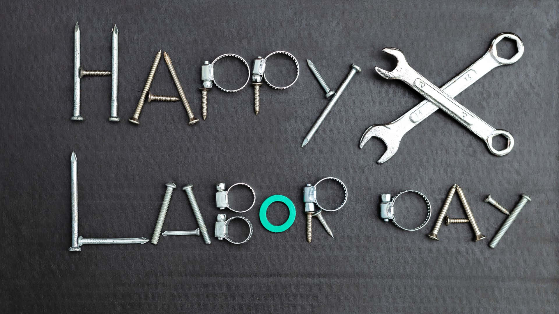 勞動節 桌布 壁紙 — 在深色紋理表面上用釘子、螺栓和扳手拼出的「HAPPY LABOR DAY」字樣。
