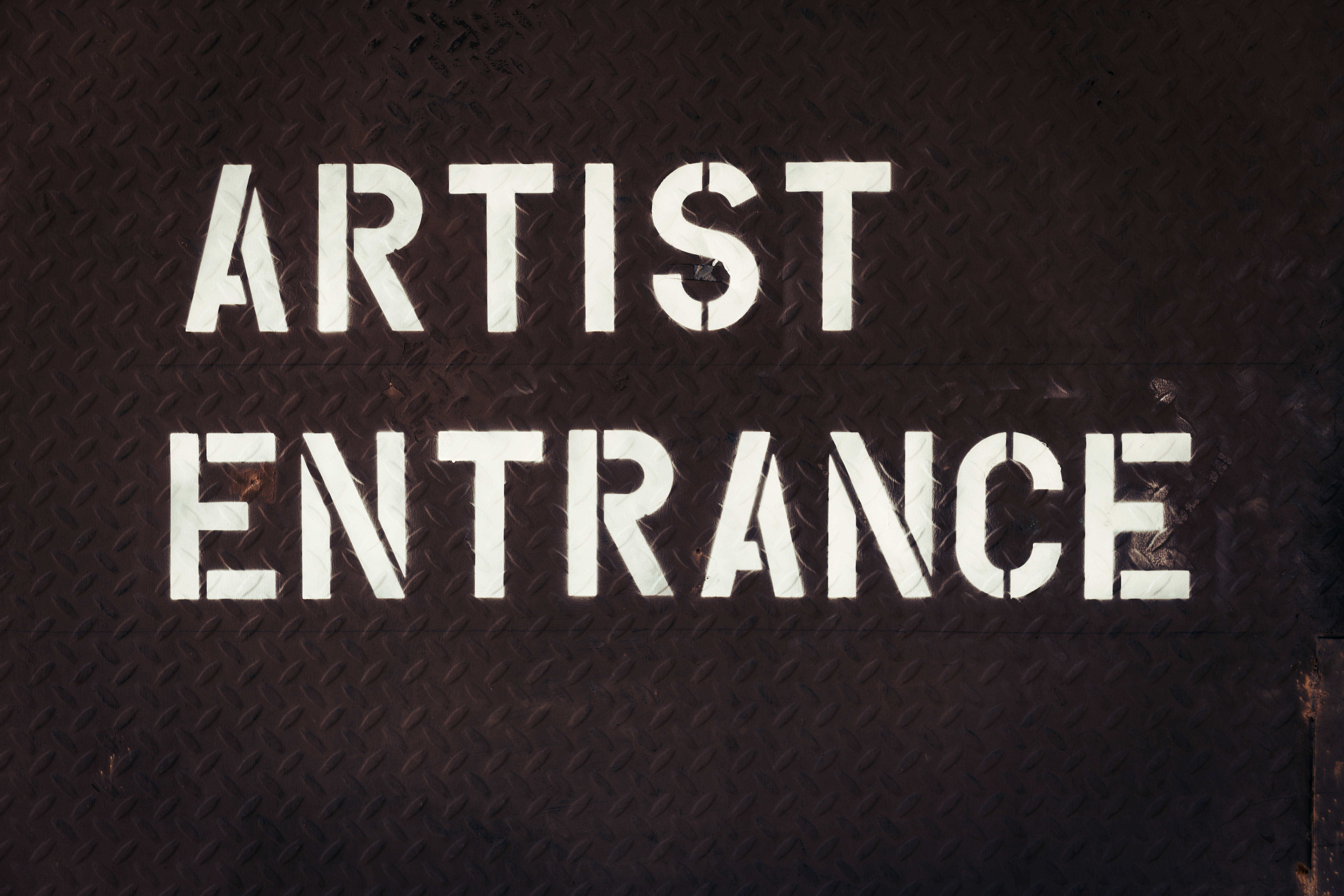 Typography 桌布 壁紙 — 在深色紋理金屬表面上，粗體白色模板文字寫著 artist entrance。