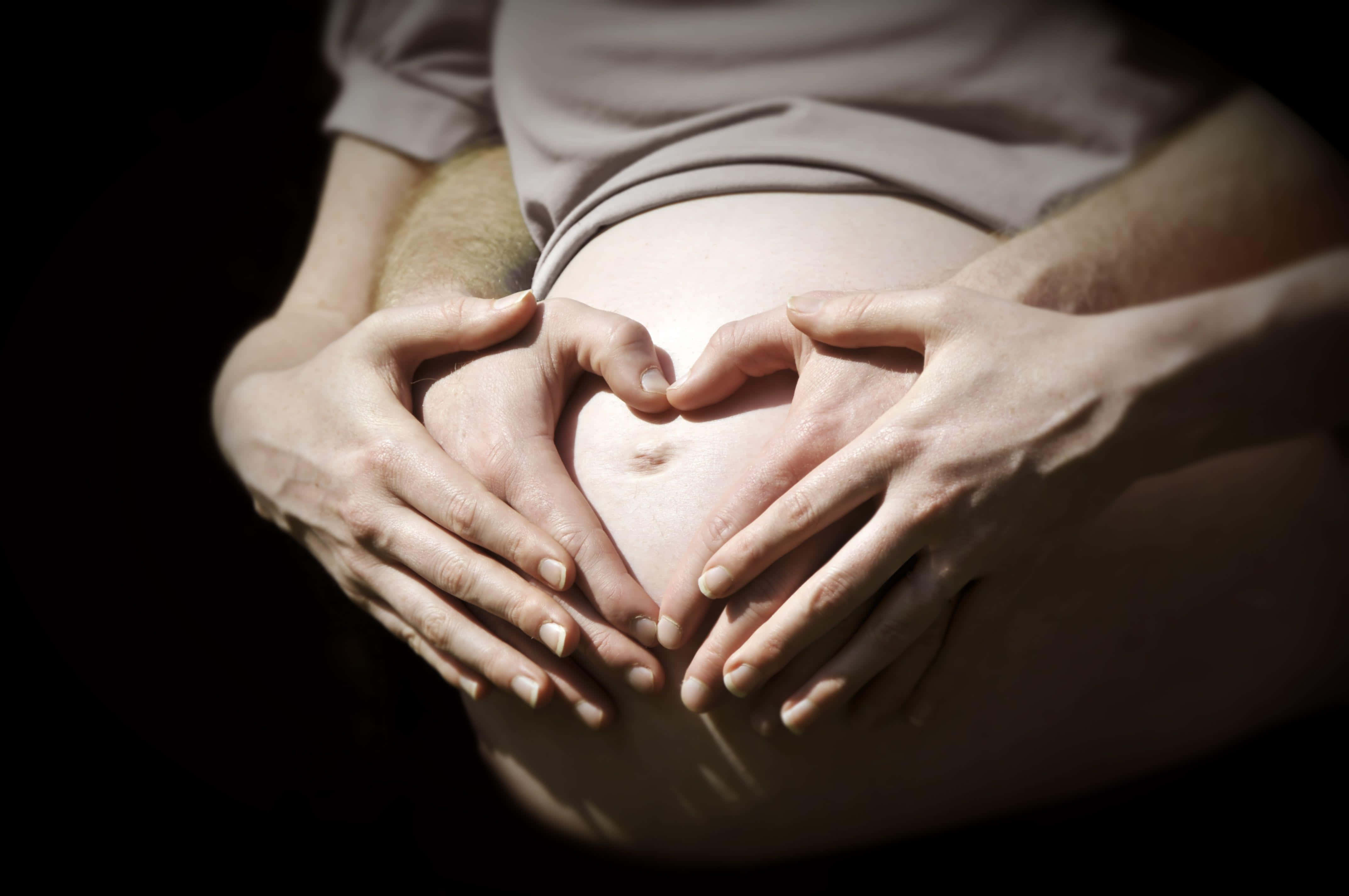 Pregnant 桌布 壁紙 — 在深色背景下，兩隻手形成心形托住懷孕的肚子。