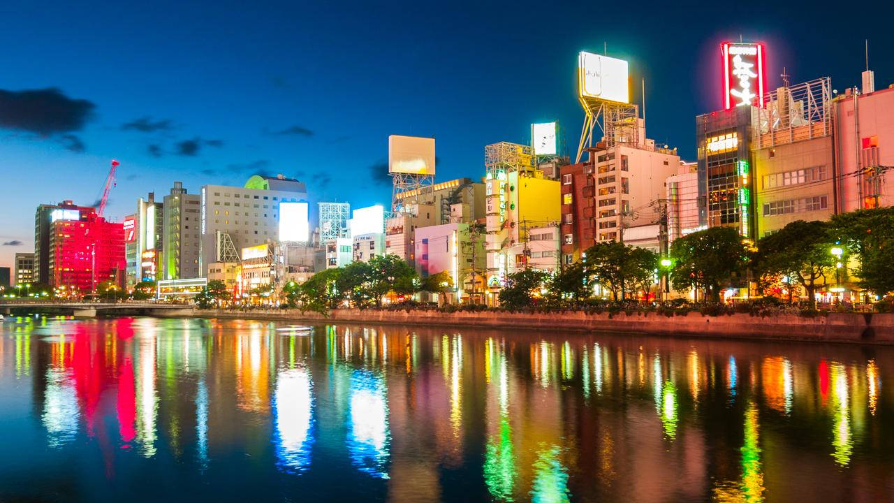 Fukuoka 桌布 壁紙 — 在深藍色天空下，充滿活力的城市天際線於黃昏時分，霓虹招牌倒映在平靜的河水上。