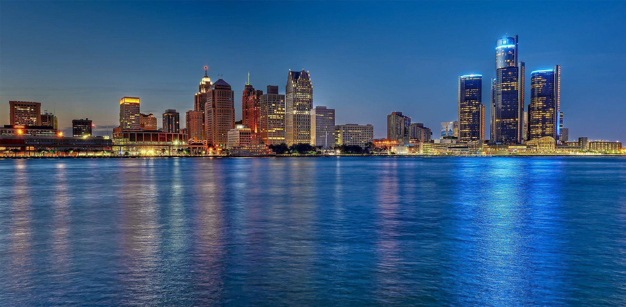 detroit 桌布 壁紙 — 在深藍色天空下，寧靜水面倒映著燈火輝煌的摩天大樓，令人驚嘆的黃昏城市景觀。