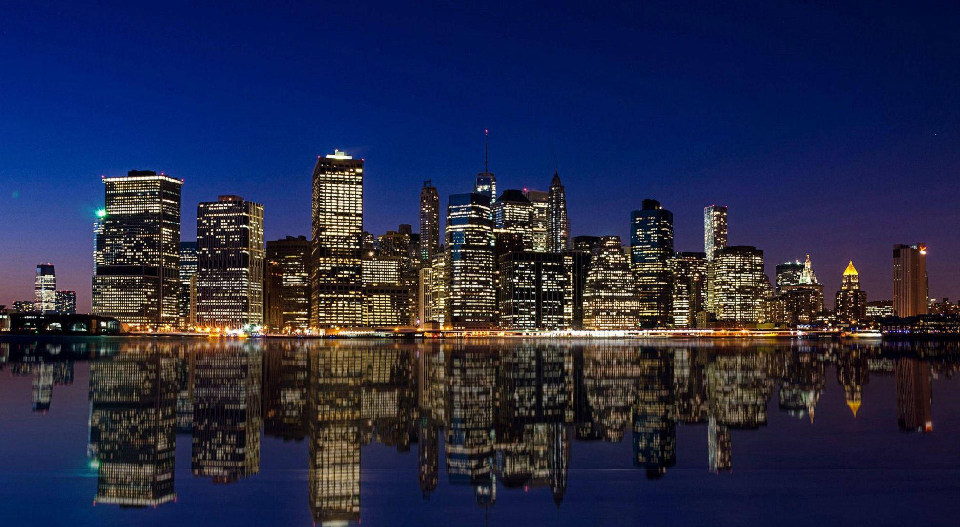 New York 桌布 壁紙 — 在深藍色天空下，燈火通明的摩天大樓完美倒映在平靜水面上，構成迷人的夜景。