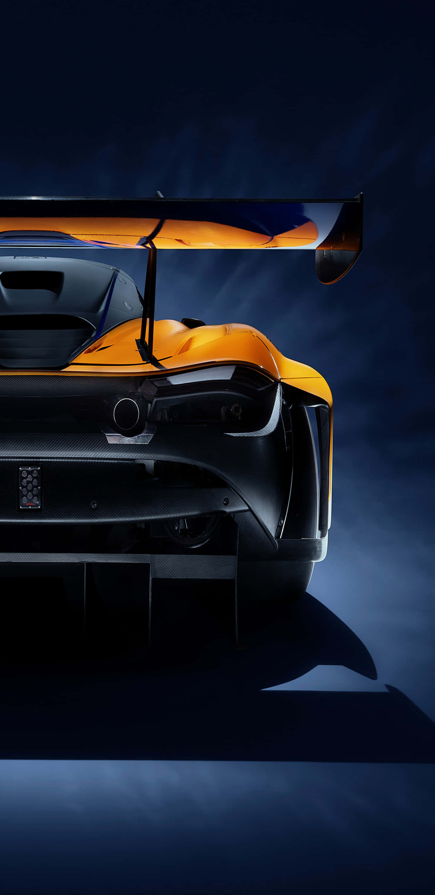 Pixel 3xl Mclaren 720s 桌布 壁紙 — 在深藍色工作室背景下，一輛時尚的橙色和黑色跑車後視圖，帶有大型尾翼，光線照亮。