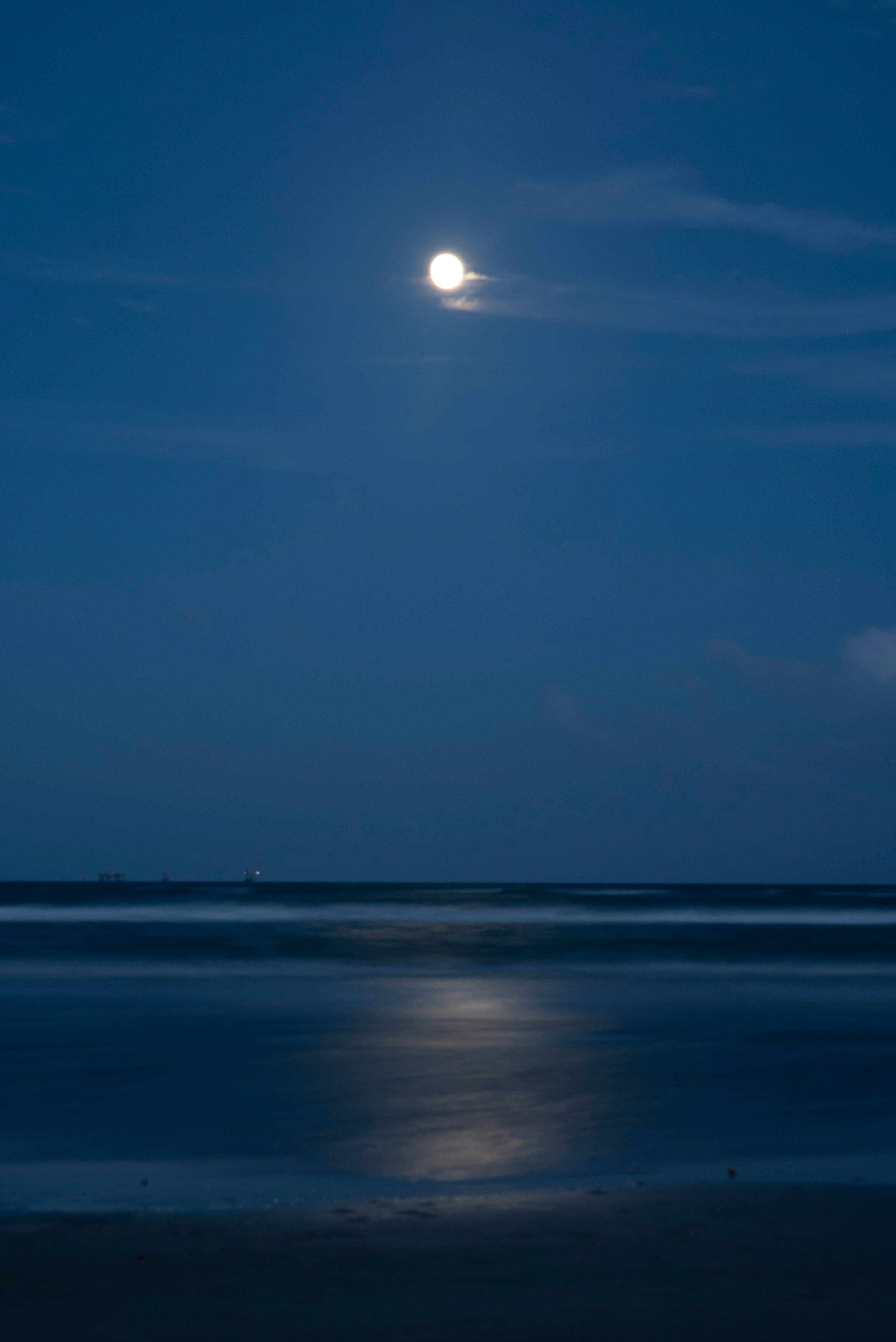 Beautiful Full Moon 桌布 壁紙 — 在深藍色暮色天空下，明亮的滿月在平靜的海浪上投射出閃爍的倒影，營造出寧靜的月光海灘場景。