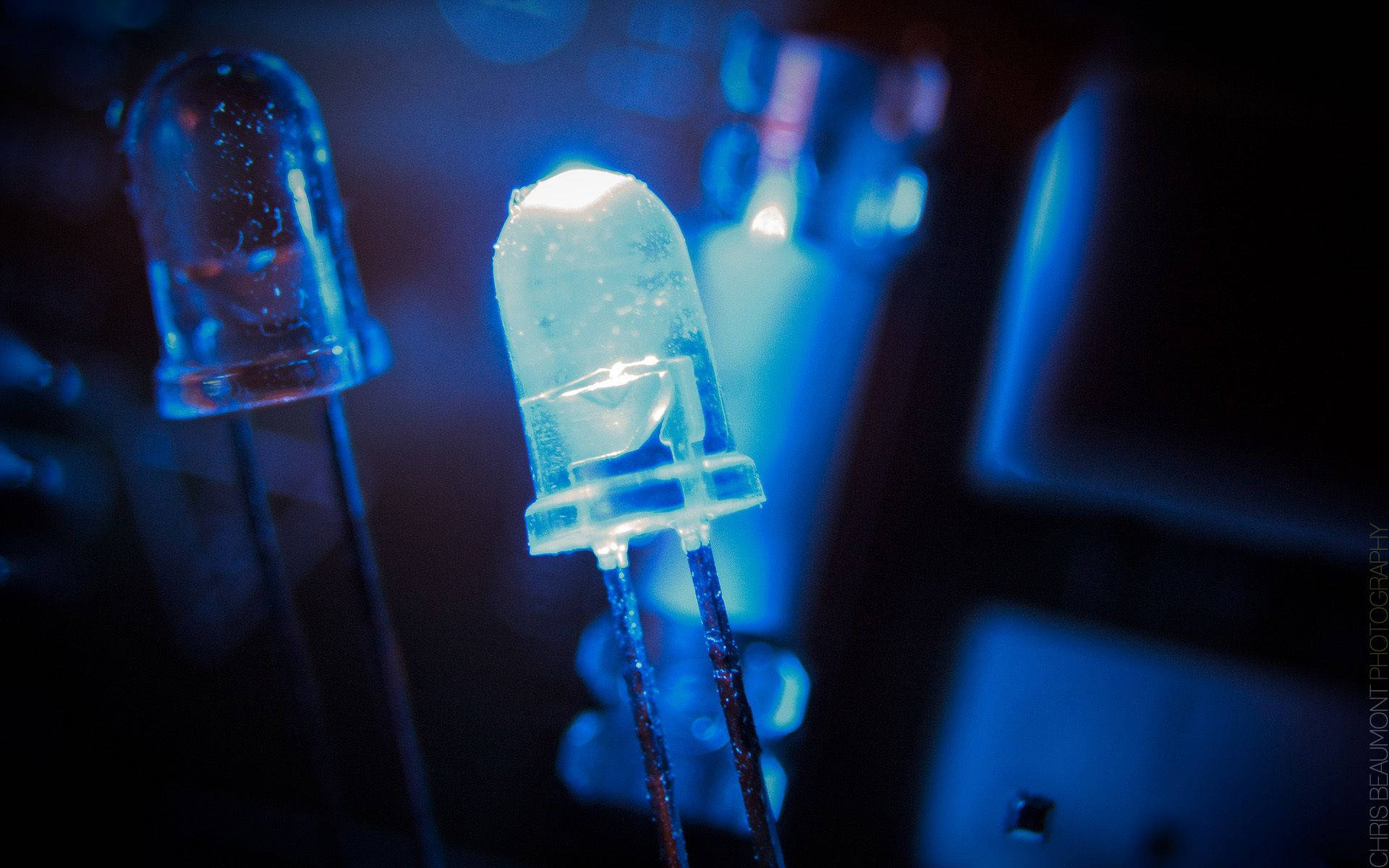Electronics 桌布 壁紙 — 在深藍色照明環境中，一顆發光的藍色LED燈泡清晰對焦，背景有模糊的科技組件。