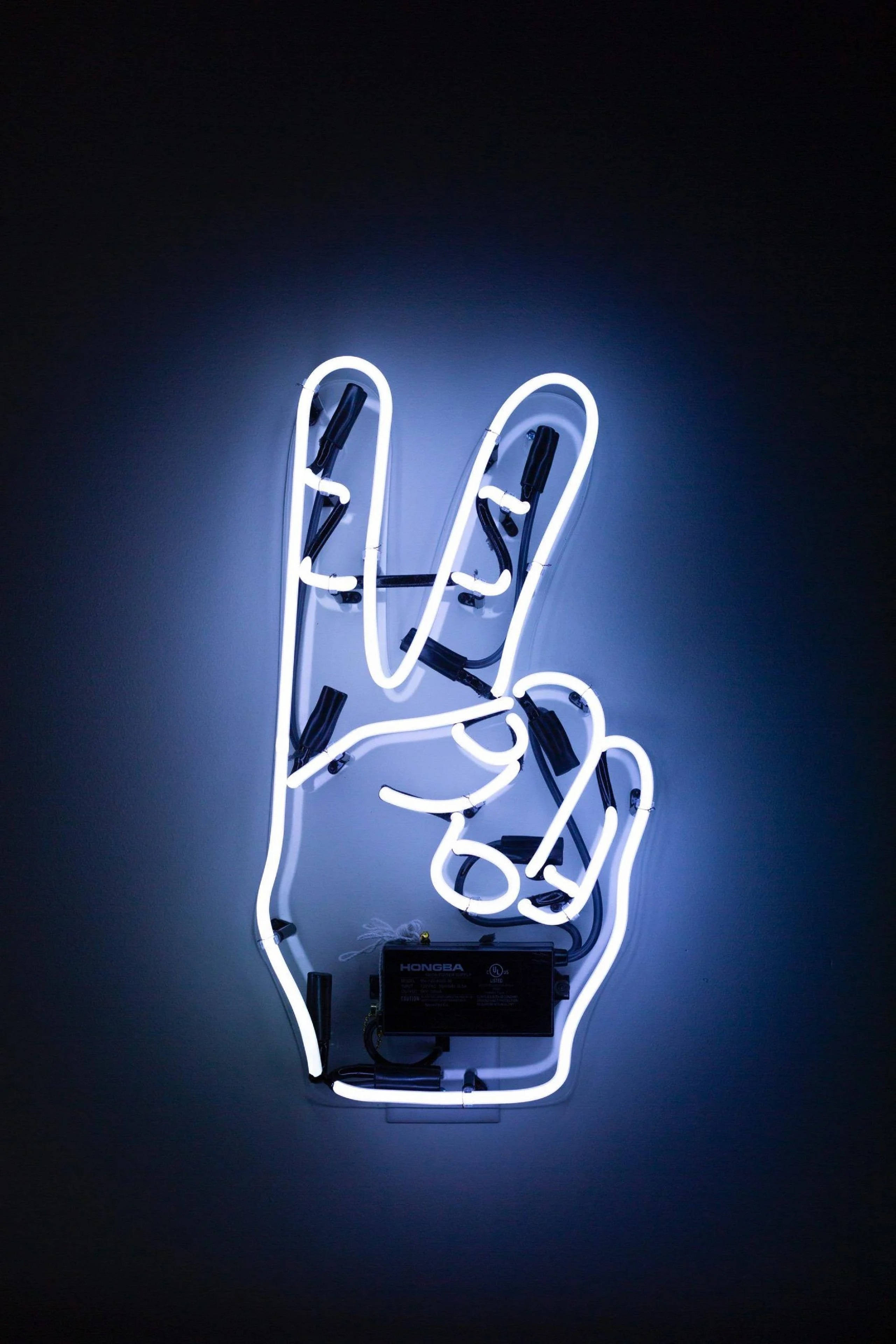 Peace 桌布 壁紙 — 在深藍色牆壁上，一個發光的白色霓虹燈牌，形狀像和平手勢。