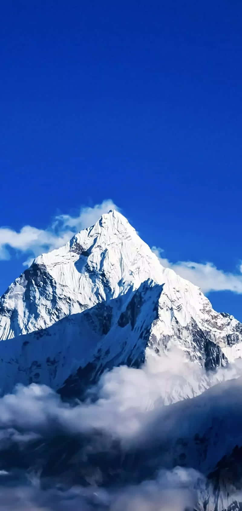Himalaya 桌布 壁紙 — 在深藍色的天空下，一座雄偉的雪山峰頂穿破雲層。