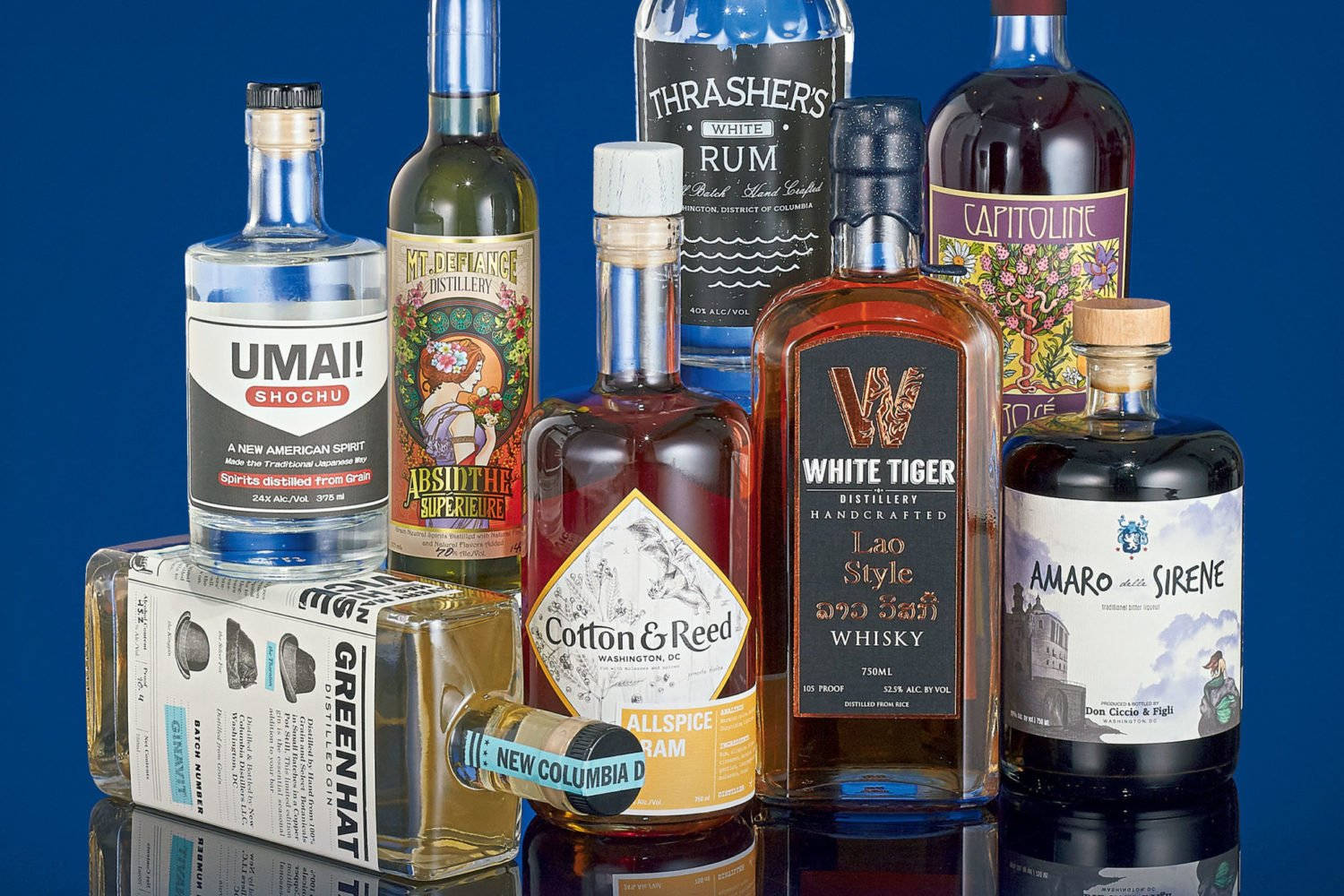 Whiskey 桌布 壁紙 — 在深藍色背景和反光表面上展示的一系列充滿活力的手工烈酒和利口酒。